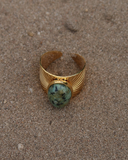 Gouden statement ring van stainless steel met grote ovaalvormige groen gemarmerde steen en subtiel streepjesreliëf in de band.