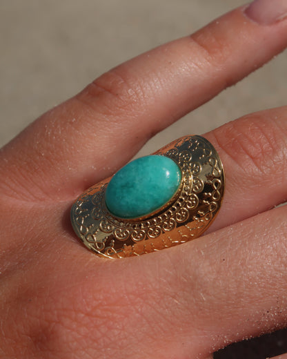 Gouden verstelbare ring met ovale vorm en grote blauwe steen, omringd door sierlijke detail.