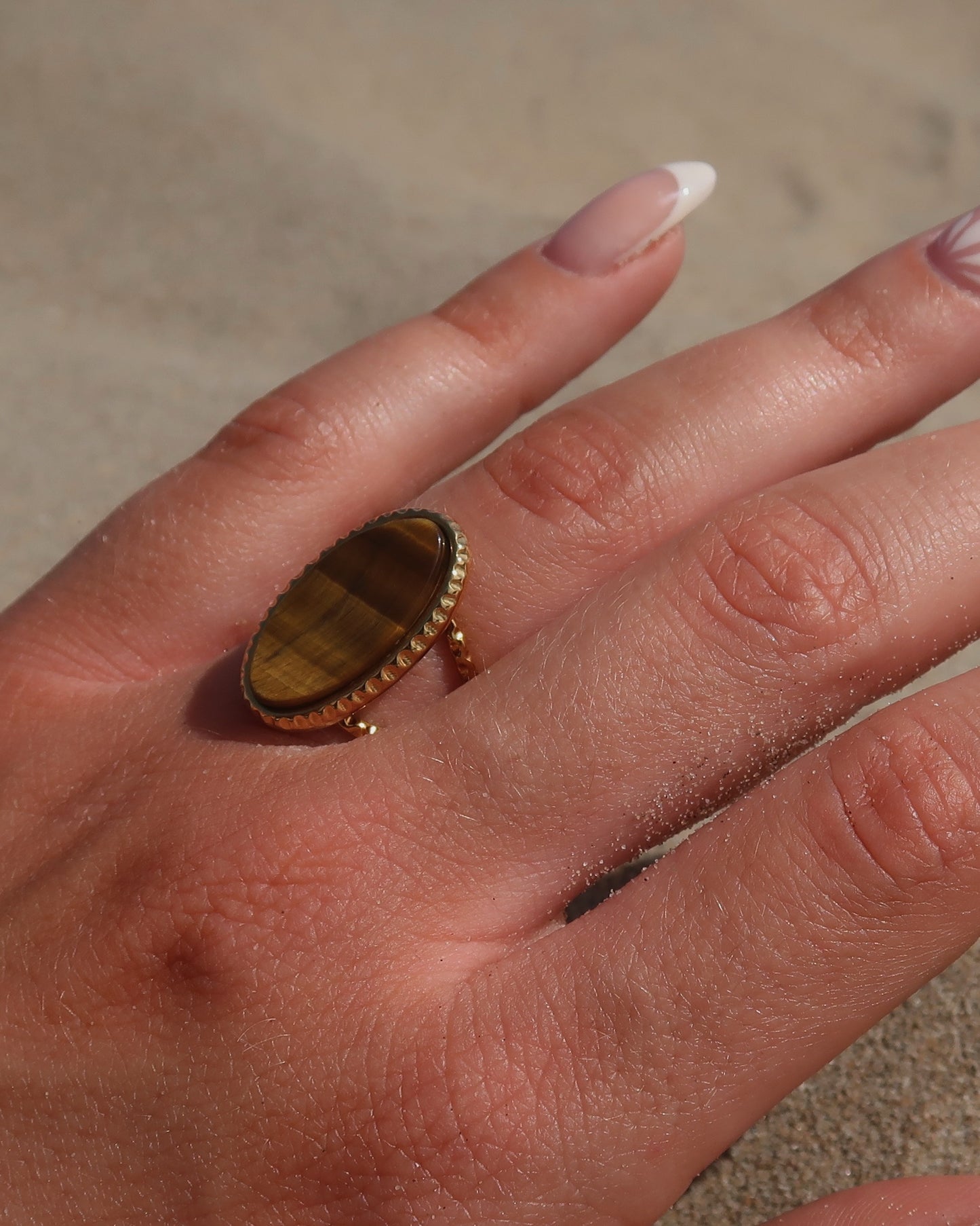 Gouden statement ring van stainless steel met een grote ovale bruine steen en een band met fijn reliëf rondom de steen.