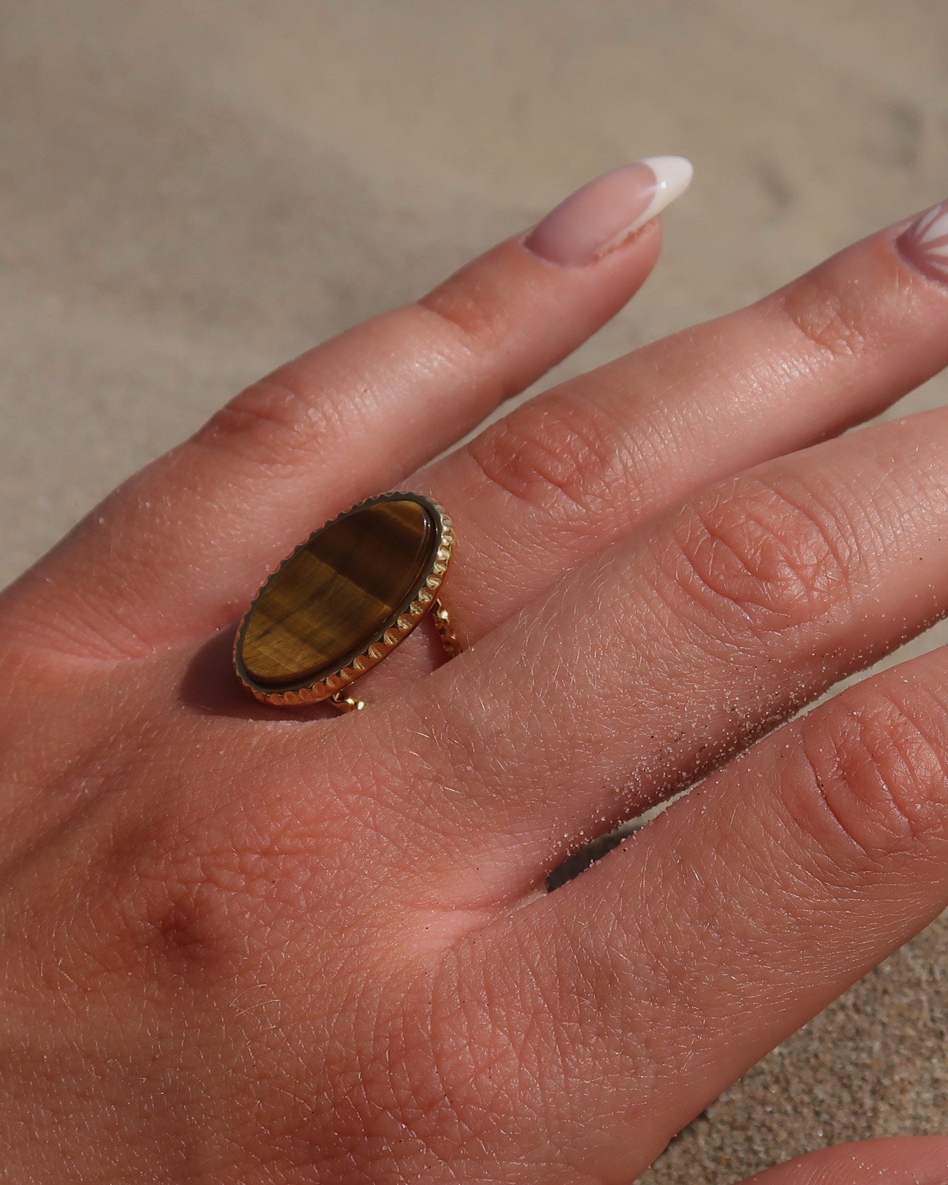 Gouden statement ring van stainless steel met een grote ovale bruine steen en een band met fijn reliëf rondom de steen.