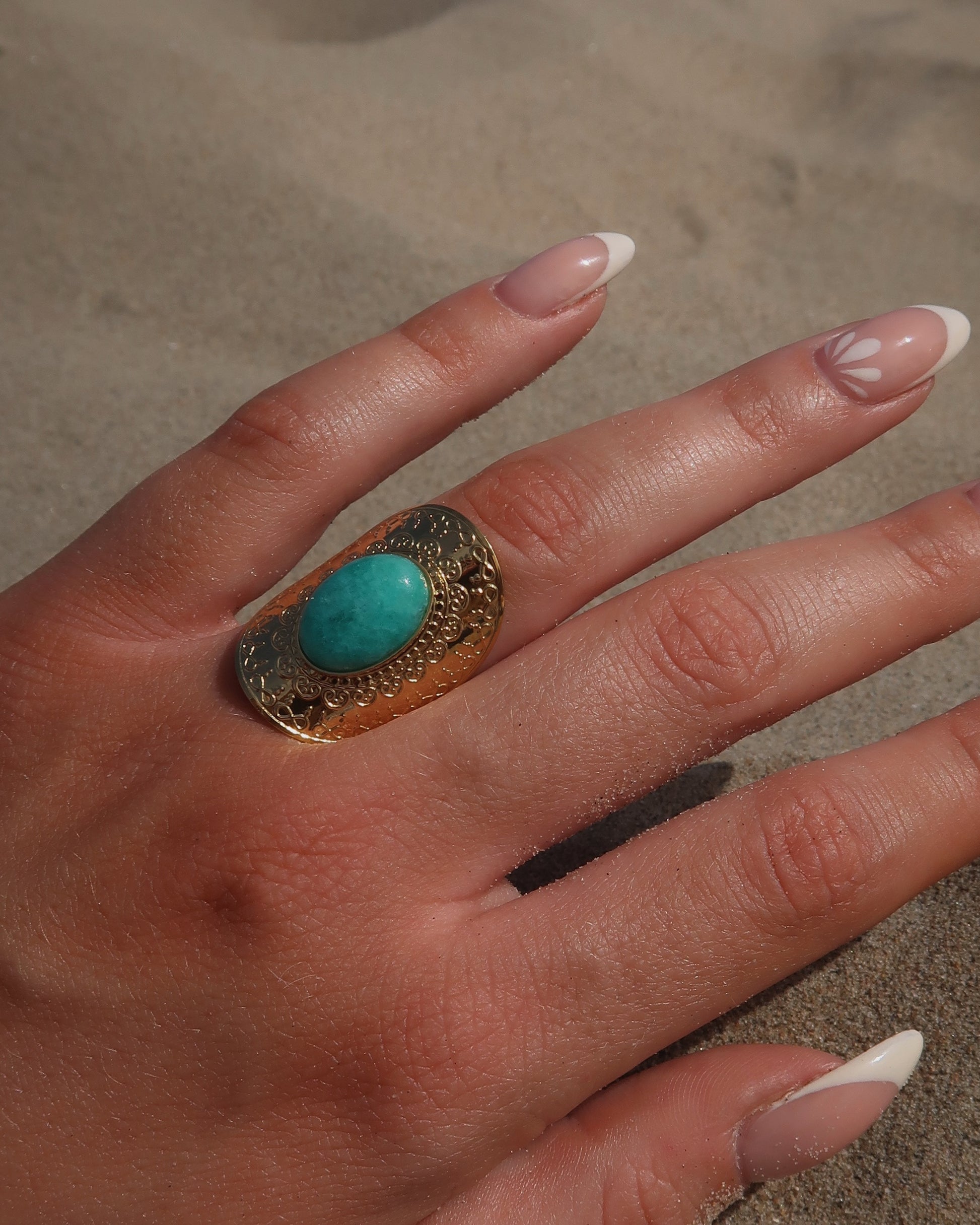 Gouden verstelbare ring met ovale vorm en grote blauwe steen, omringd door sierlijke detail.