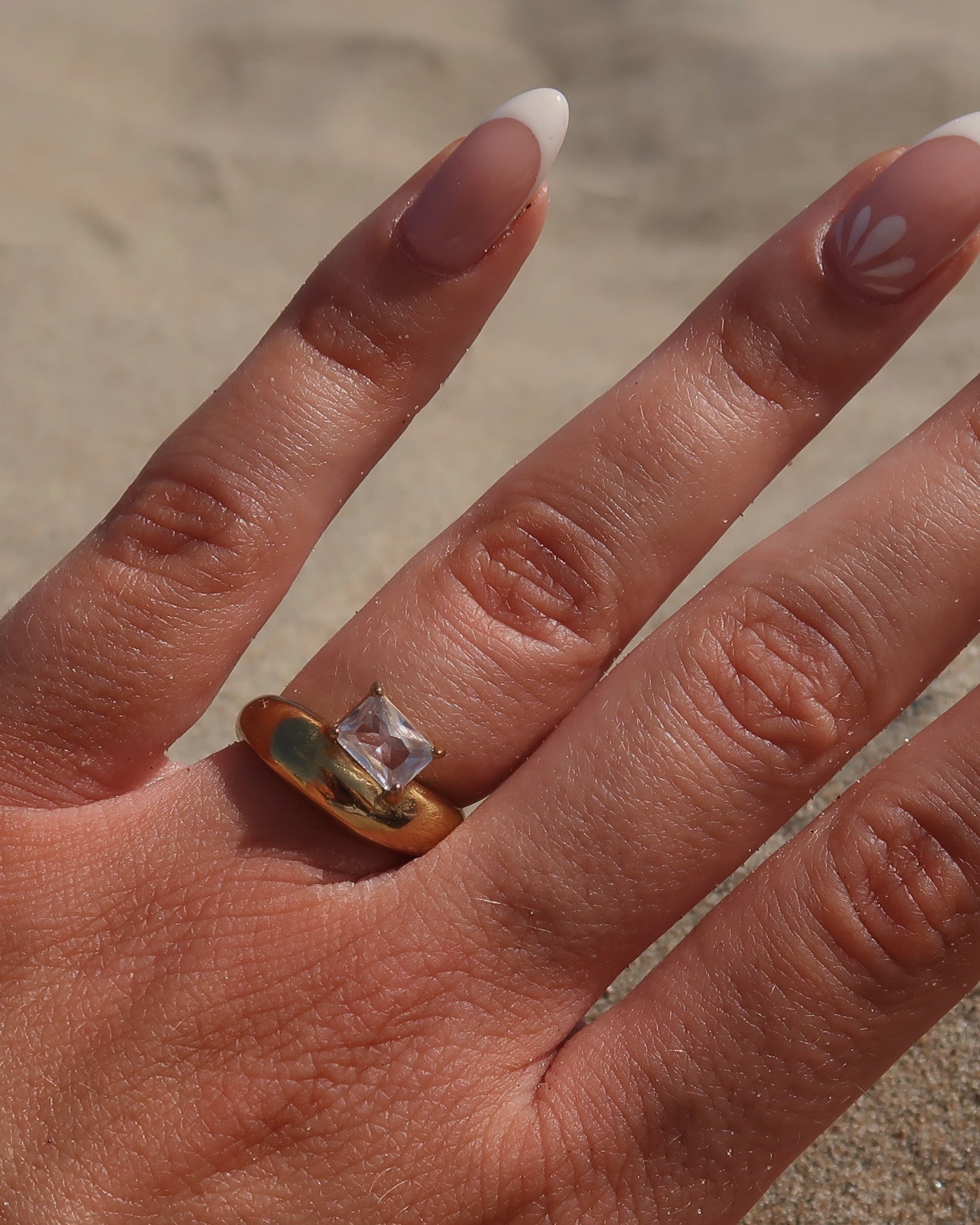 Gouden ring met glad design en een zilverkleurige steen aan de bovenzijde, gemaakt van waterproof stainless steel.