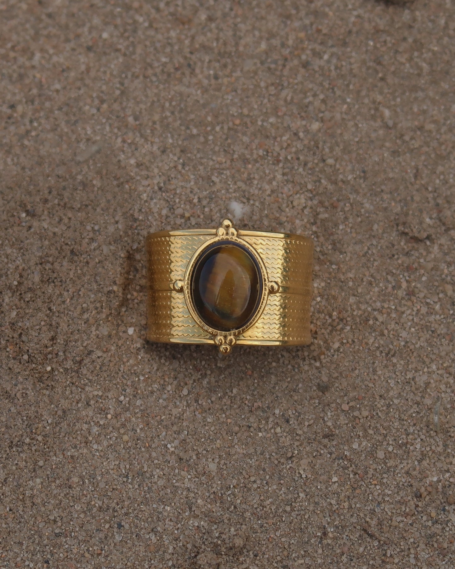 Gouden verstelbare ring van stainless steel met ovale bruine steen en verfijnde details rondom de band.