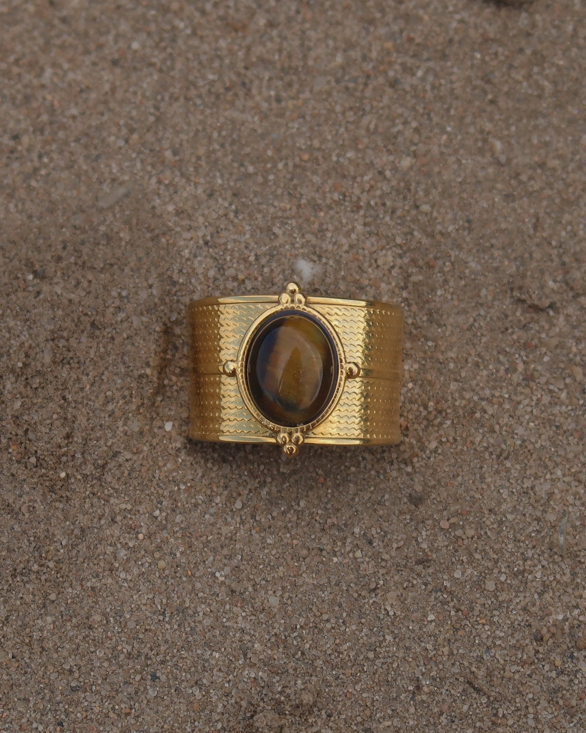 Gouden verstelbare ring van stainless steel met ovale bruine steen en verfijnde details rondom de band.