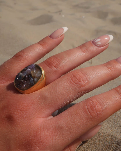 Grote gouden ring van stainless steel met een gladde band en een rechthoekig vlak gevuld met lichtpaarse amethist-achtige steentjes