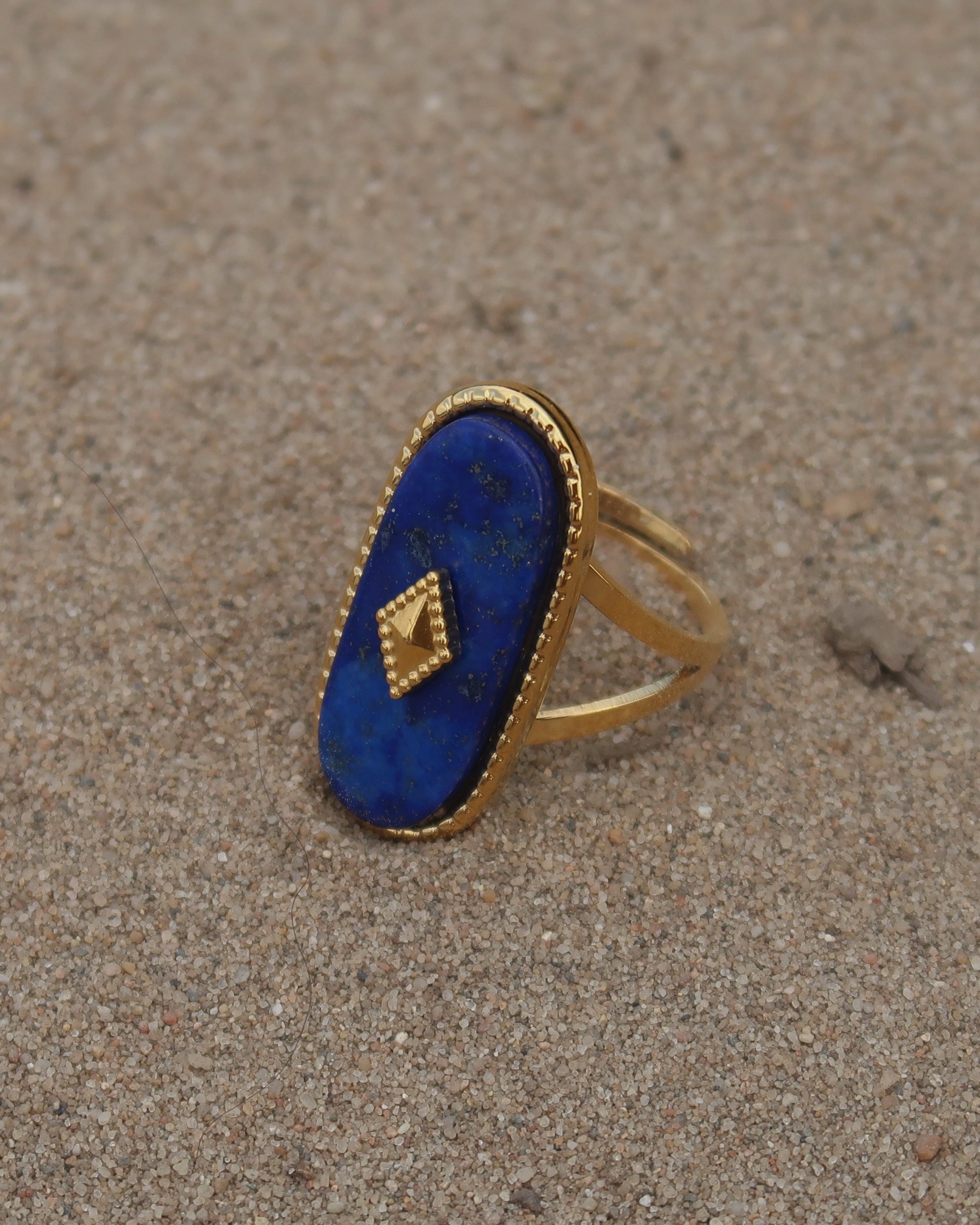 Gouden stainless steel verstelbare ring met een grote donkerblauwe ovale steen, een gouden ruit in het midden en verfijnde details rondom
