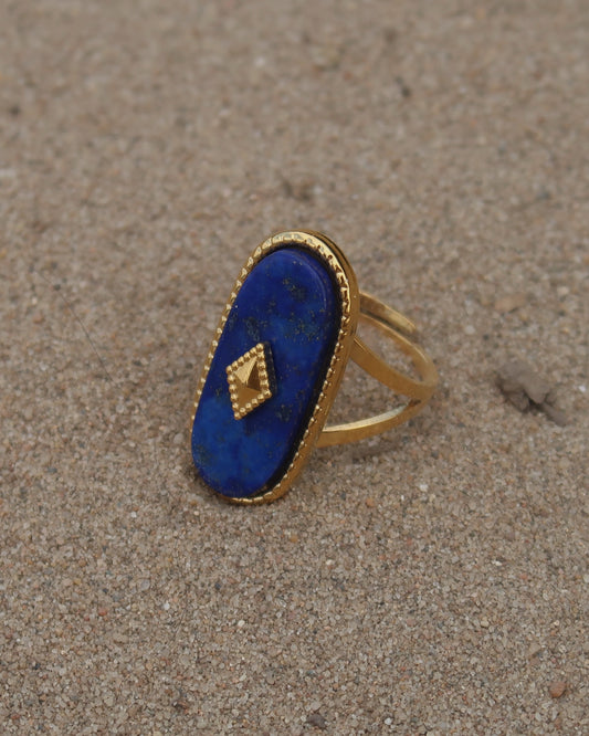 Gouden stainless steel verstelbare ring met een grote donkerblauwe ovale steen, een gouden ruit in het midden en verfijnde details rondom
