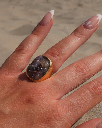 Grote gouden ring van stainless steel met een gladde band en een rechthoekig vlak gevuld met lichtpaarse amethist-achtige steentjes