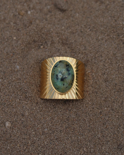 Gouden statement ring van stainless steel met grote ovaalvormige groen gemarmerde steen en subtiel streepjesreliëf in de band.
