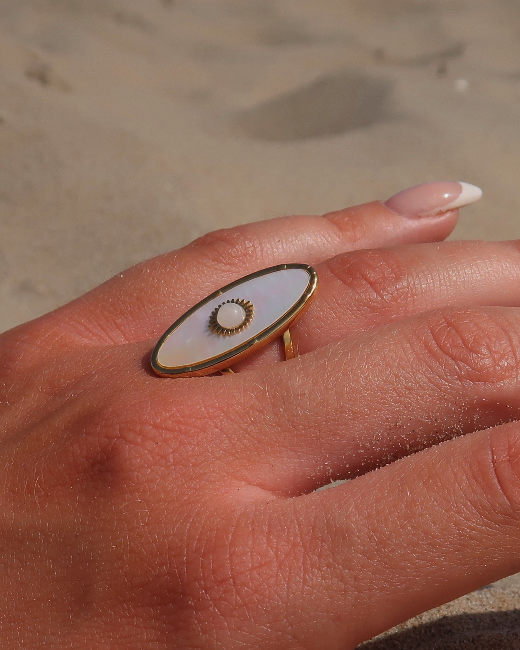 Gouden statement ring van stainless steel met ovale witte steen en parelmoerachtige afwerking, verstelbare dubbele band.