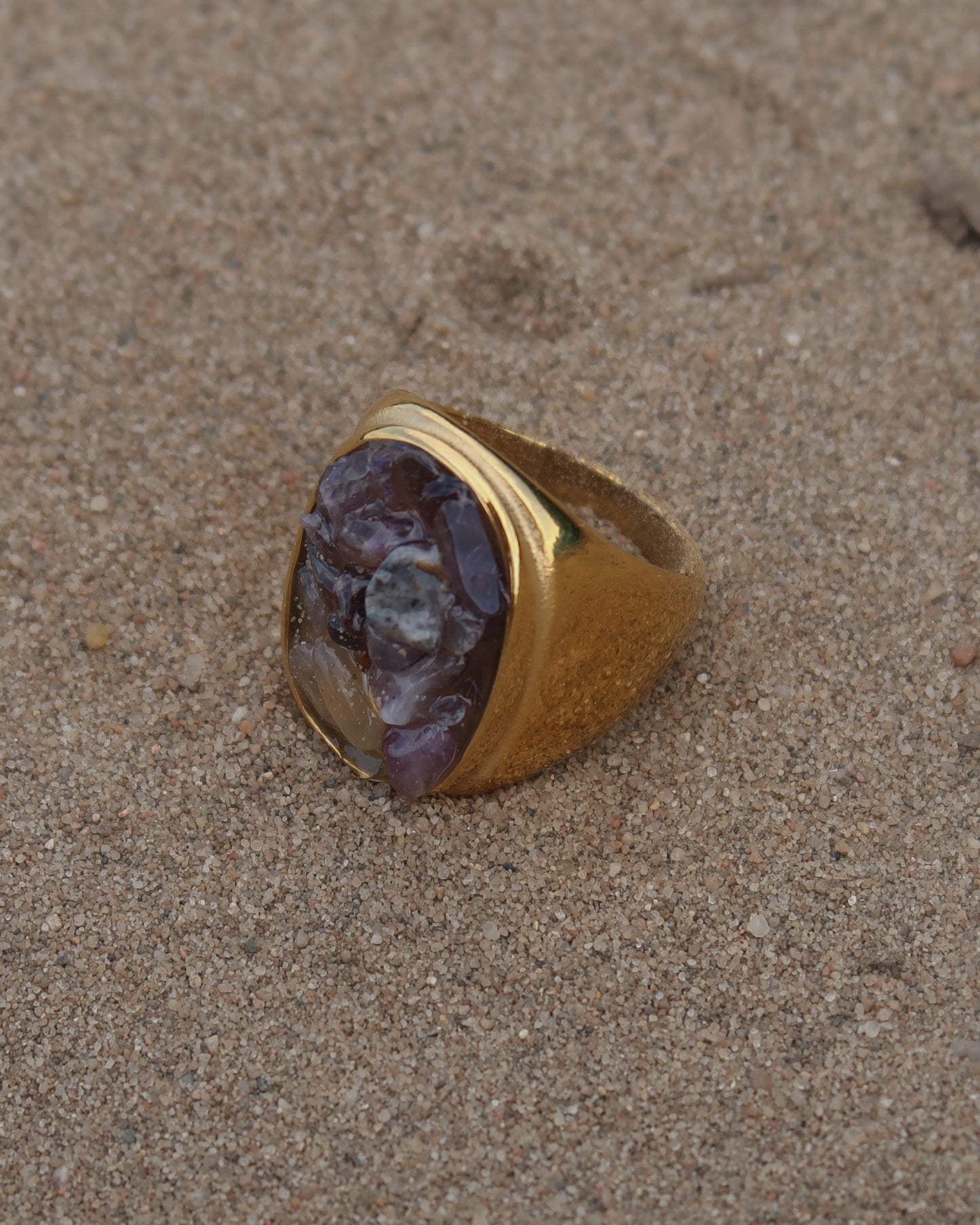 Grote gouden ring van stainless steel met een gladde band en een rechthoekig vlak gevuld met lichtpaarse amethist-achtige steentjes