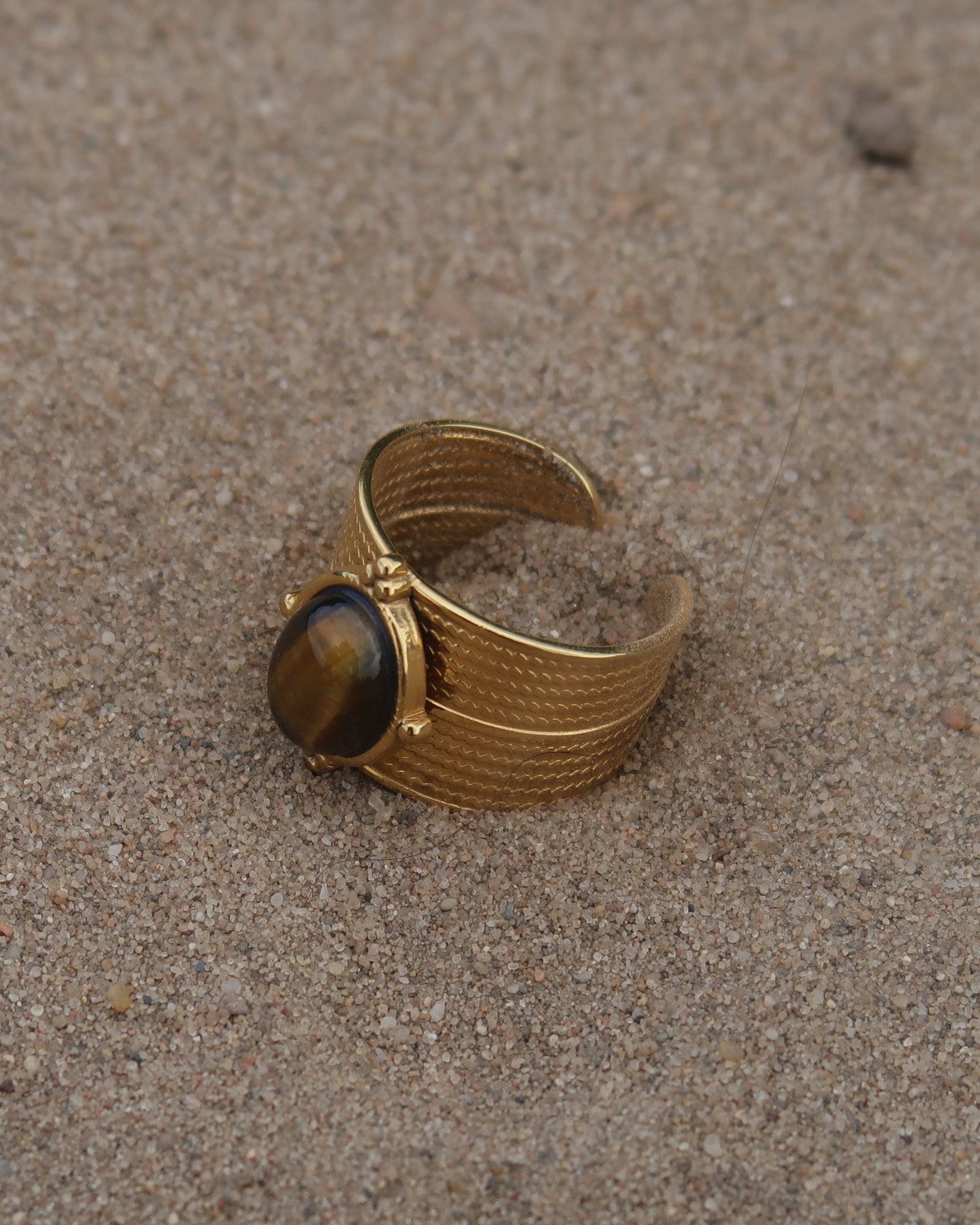 Gouden verstelbare ring van stainless steel met ovale bruine steen en verfijnde details rondom de band.