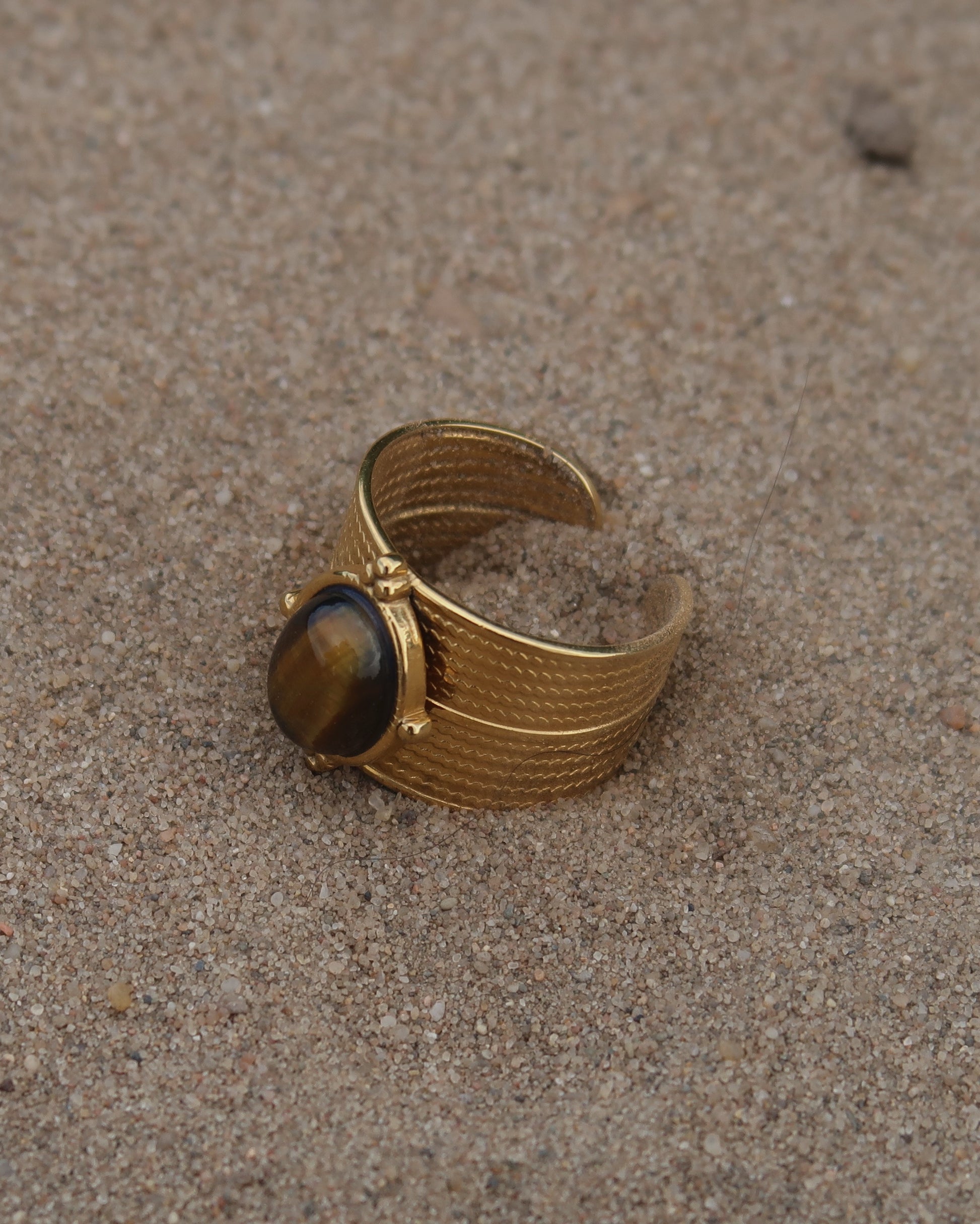 Gouden verstelbare ring van stainless steel met ovale bruine steen en verfijnde details rondom de band.