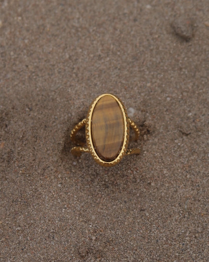 Gouden statement ring van stainless steel met een grote ovale bruine steen en een band met fijn reliëf rondom de steen.