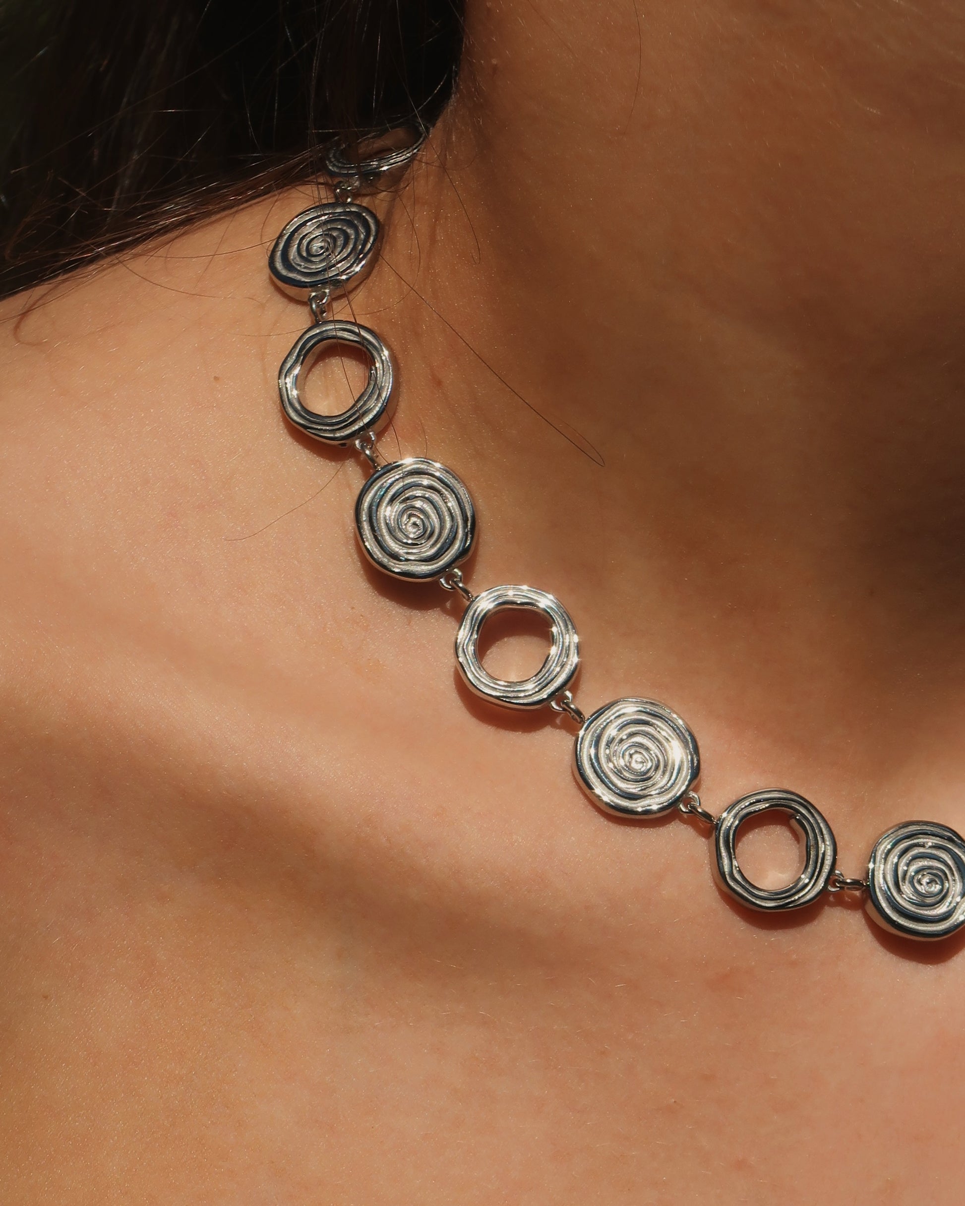 Zilveren statementketting met aaneengeschakelde ronde schelpvormen in verschillende stijlen.