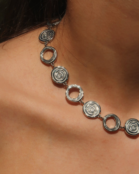 Zilveren statementketting met aaneengeschakelde ronde schelpvormen in verschillende stijlen.