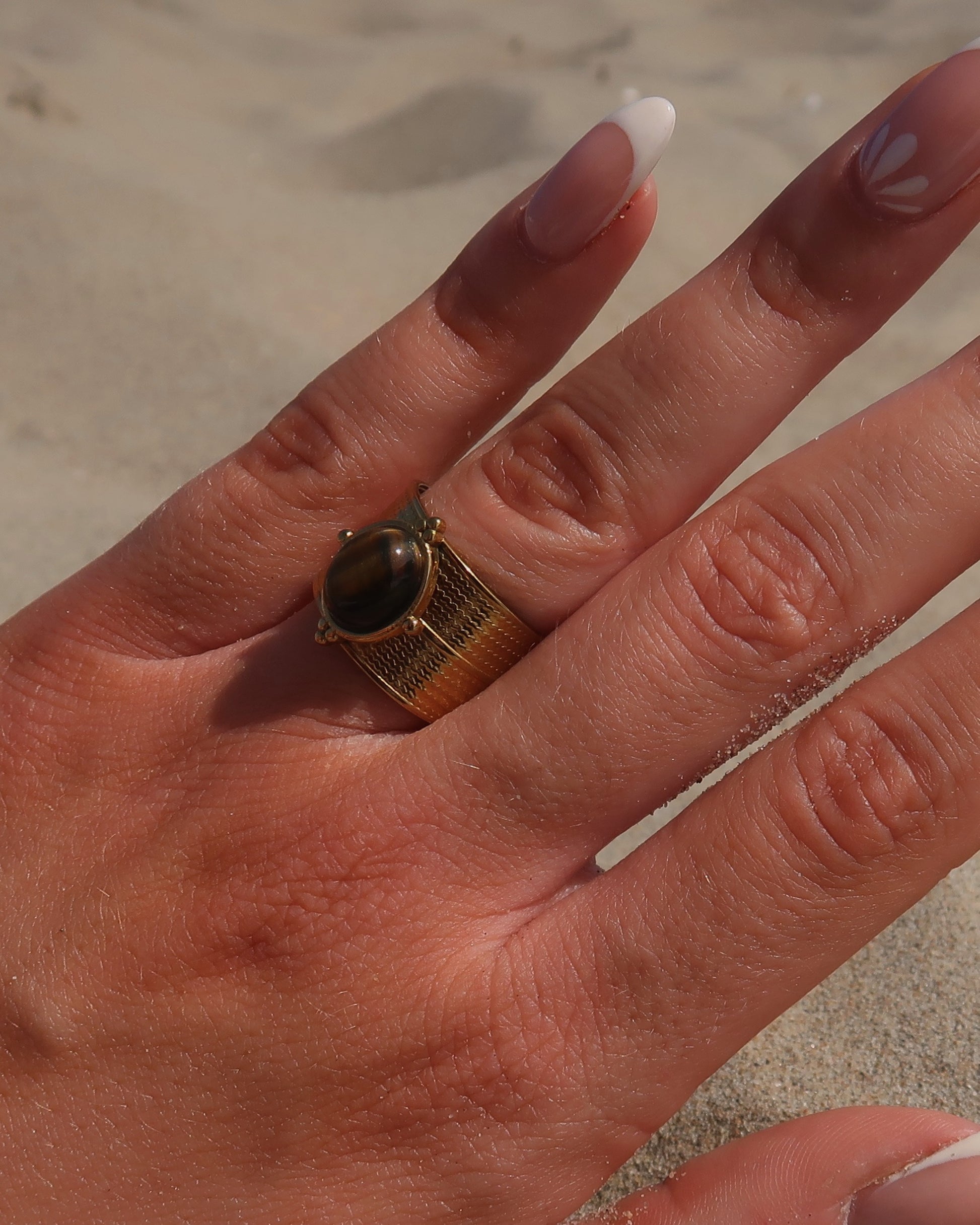 Gouden verstelbare ring van stainless steel met ovale bruine steen en verfijnde details rondom de band.