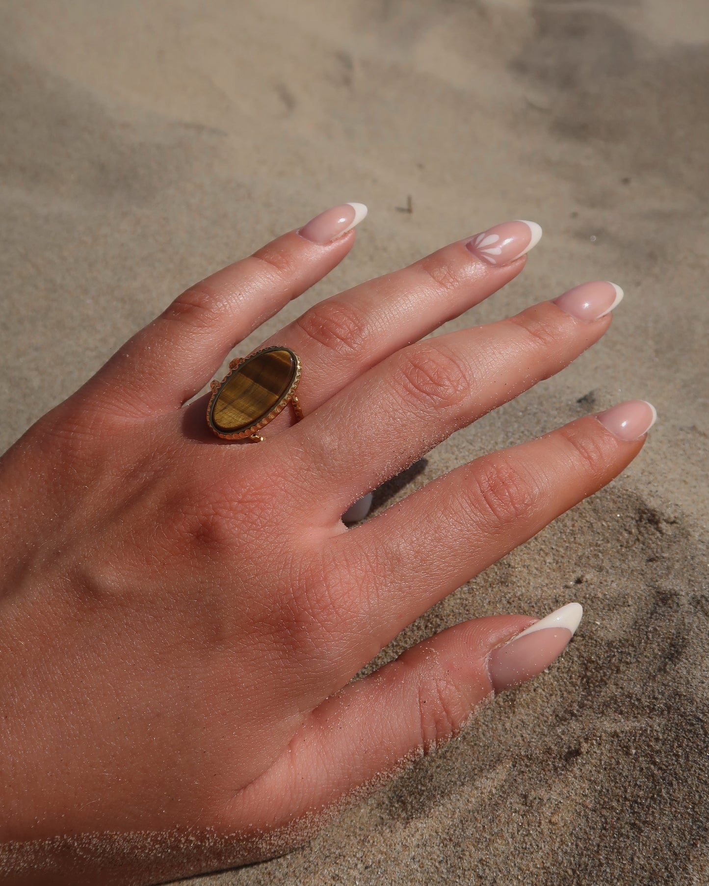 Gouden statement ring van stainless steel met een grote ovale bruine steen en een band met fijn reliëf rondom de steen.