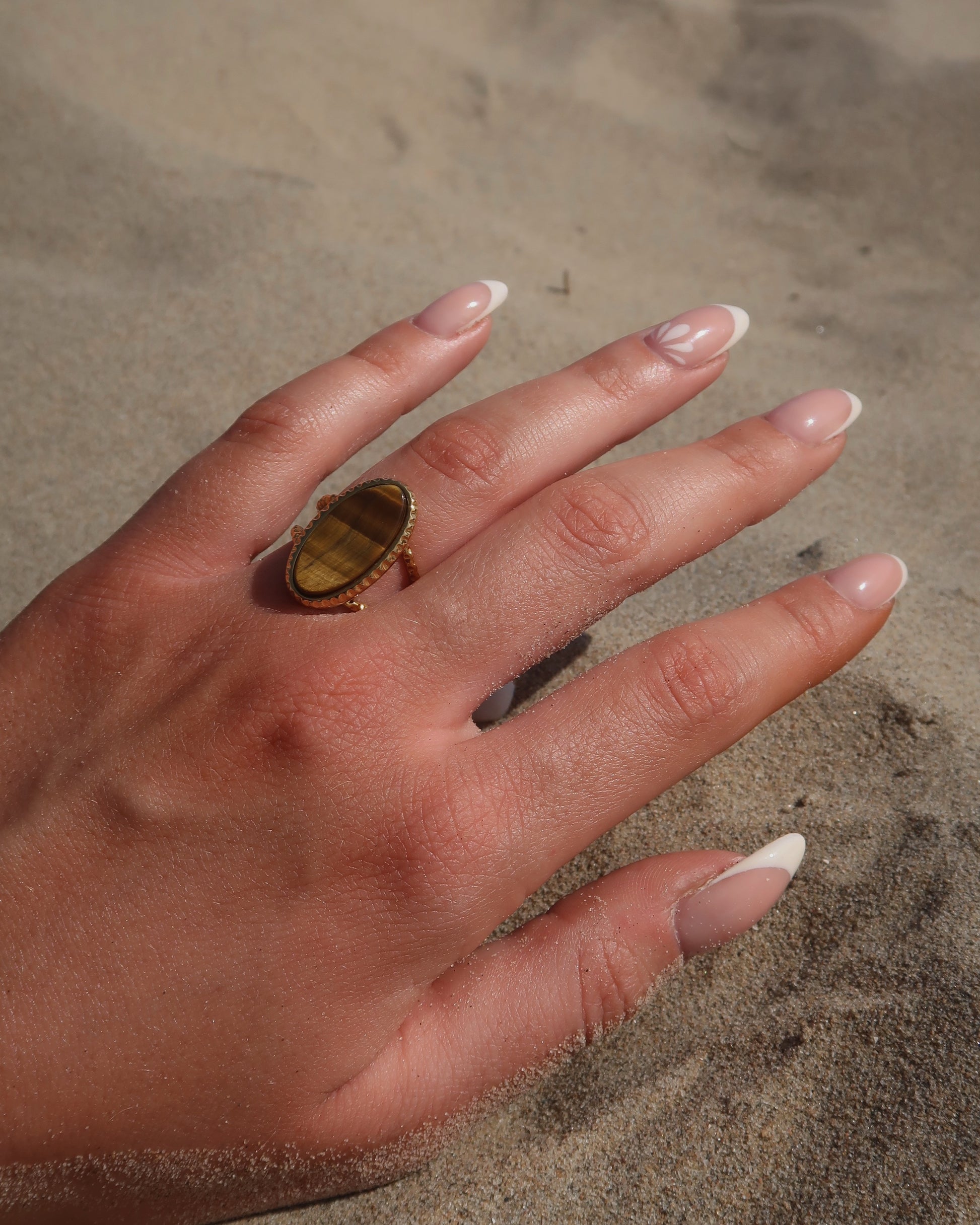 Gouden statement ring van stainless steel met een grote ovale bruine steen en een band met fijn reliëf rondom de steen.