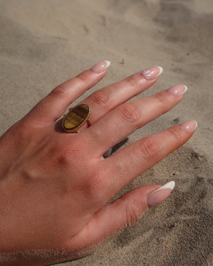 Gouden statement ring van stainless steel met een grote ovale bruine steen en een band met fijn reliëf rondom de steen.