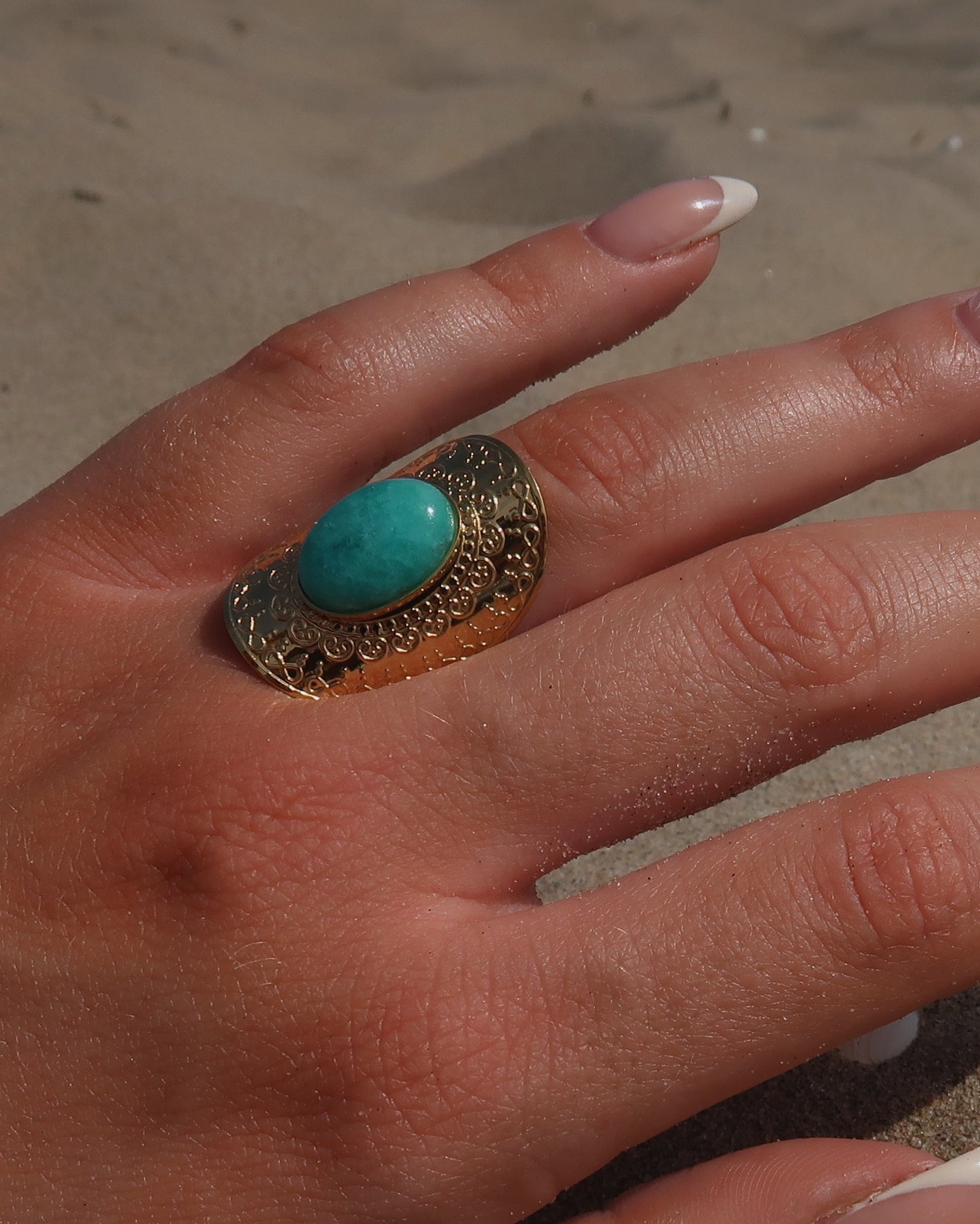 Gouden verstelbare ring met ovale vorm en grote blauwe steen, omringd door sierlijke detail.