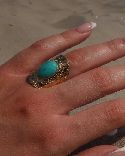Gouden verstelbare ring met ovale vorm en grote blauwe steen, omringd door sierlijke detail.