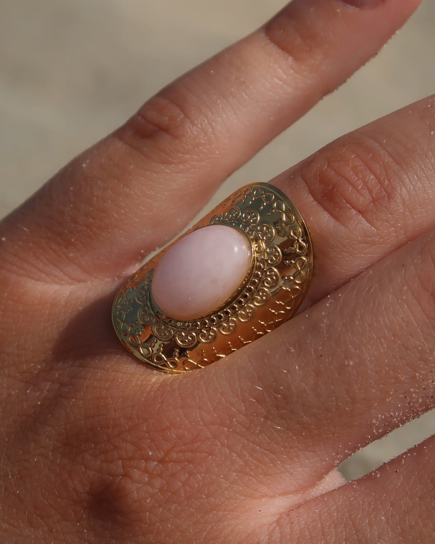 Gouden verstelbare ring met ovale vorm en grote roze steen, omringd door sierlijke details