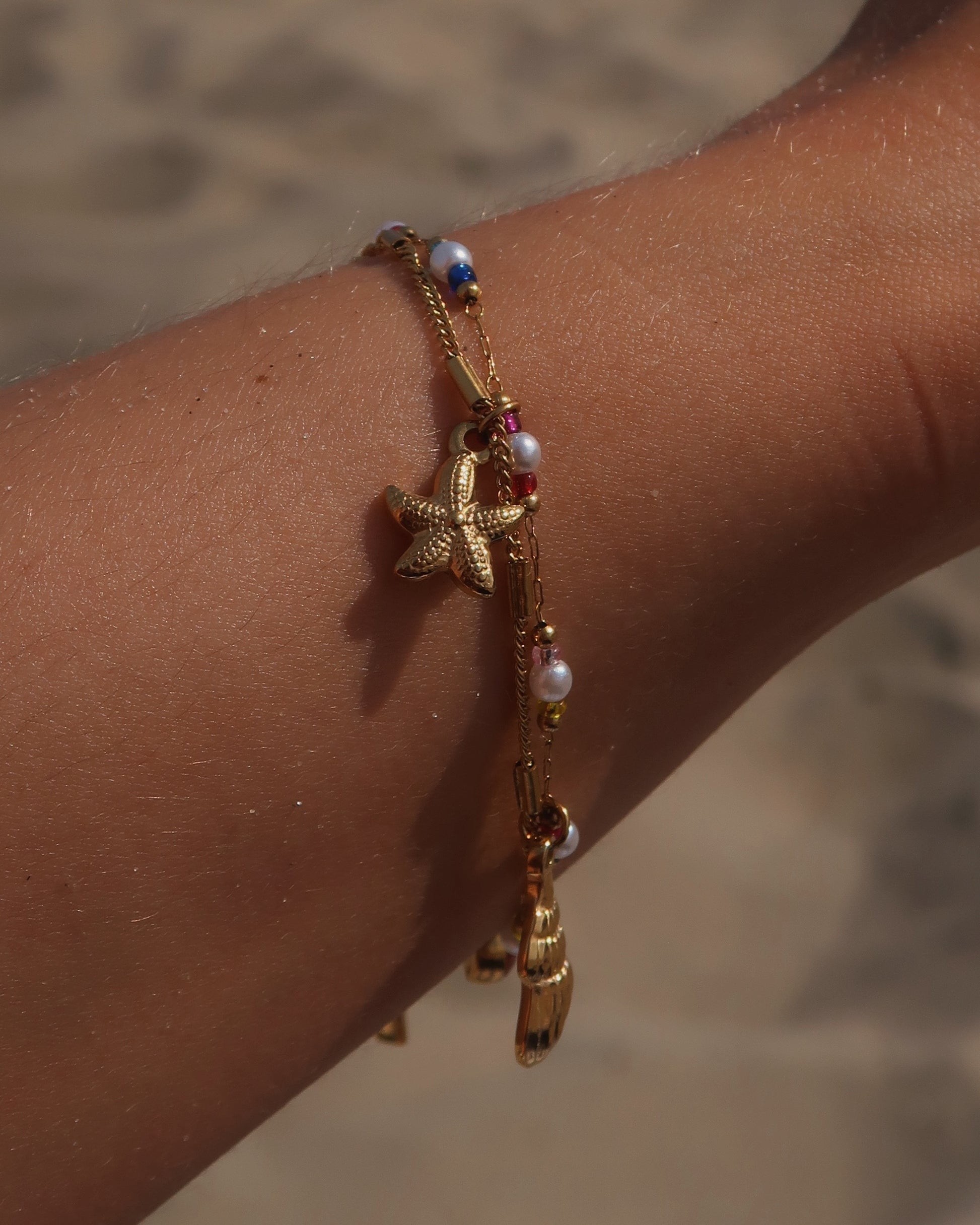 Gouden stainless steel armband met kleurrijke kraaltjes en bedels in de vorm van een schelp, zeester en roze steen – zomerse sieradenstijl.