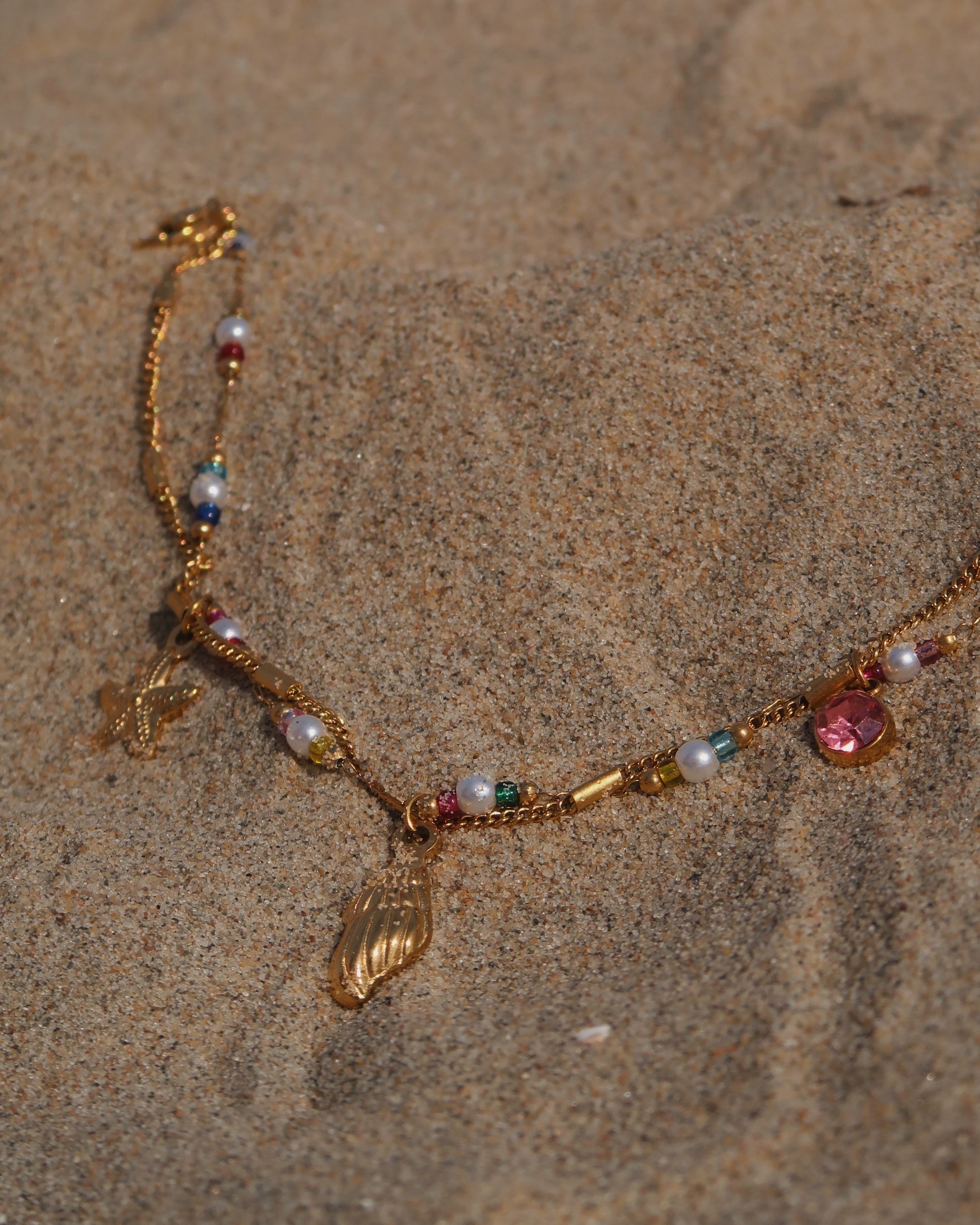 Gouden stainless steel armband met kleurrijke kraaltjes en bedels in de vorm van een schelp, zeester en roze steen – zomerse sieradenstijl.