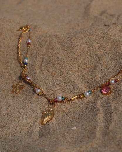 Gouden stainless steel armband met kleurrijke kraaltjes en bedels in de vorm van een schelp, zeester en roze steen – zomerse sieradenstijl.