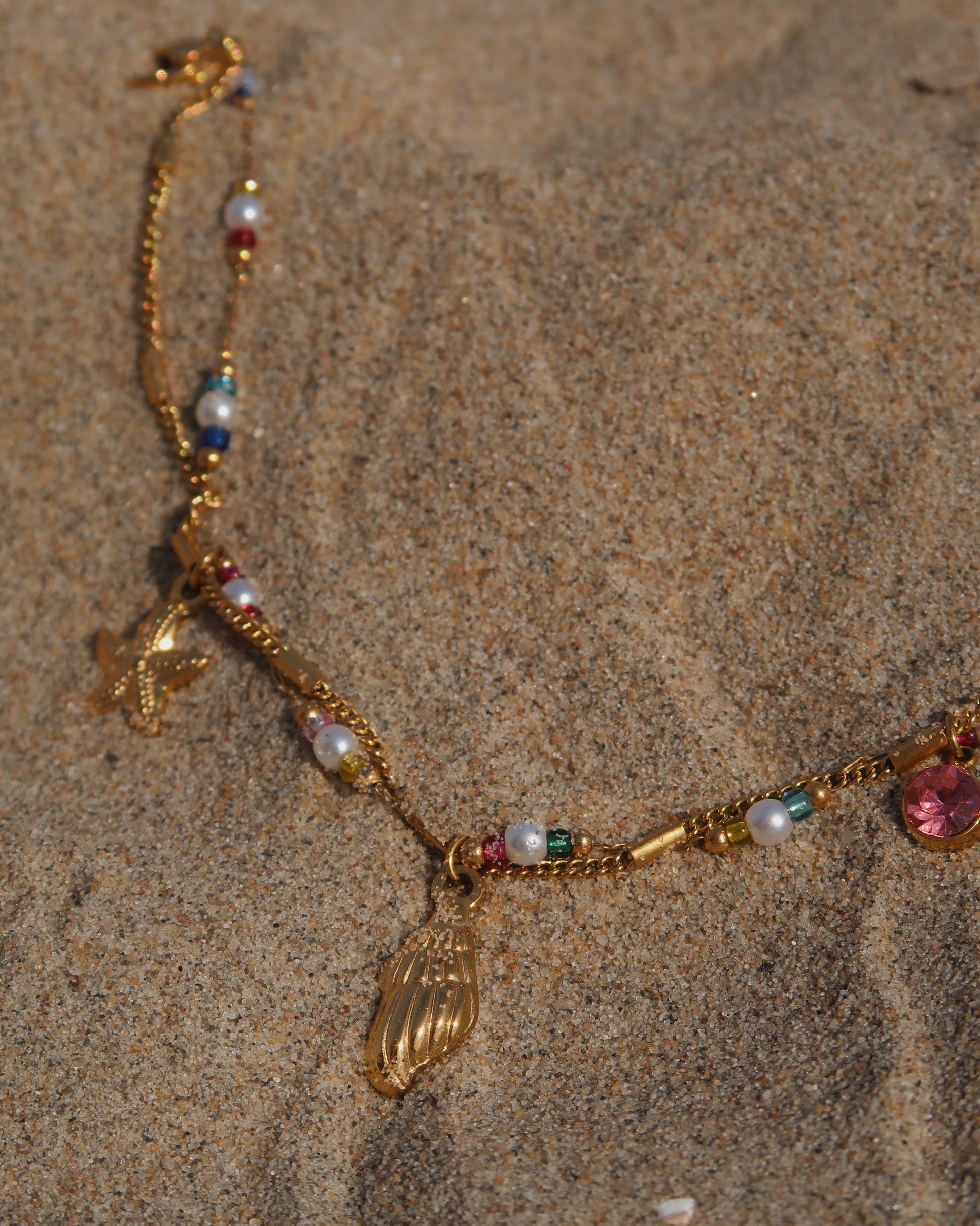 Gouden stainless steel armband met kleurrijke kraaltjes en bedels in de vorm van een schelp, zeester en roze steen – zomerse sieradenstijl.