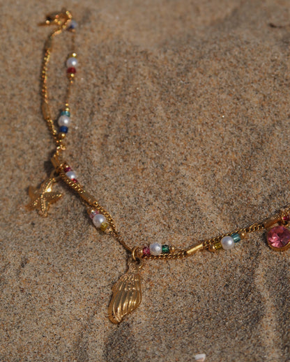 Gouden stainless steel armband met kleurrijke kraaltjes en bedels in de vorm van een schelp, zeester en roze steen – zomerse sieradenstijl.