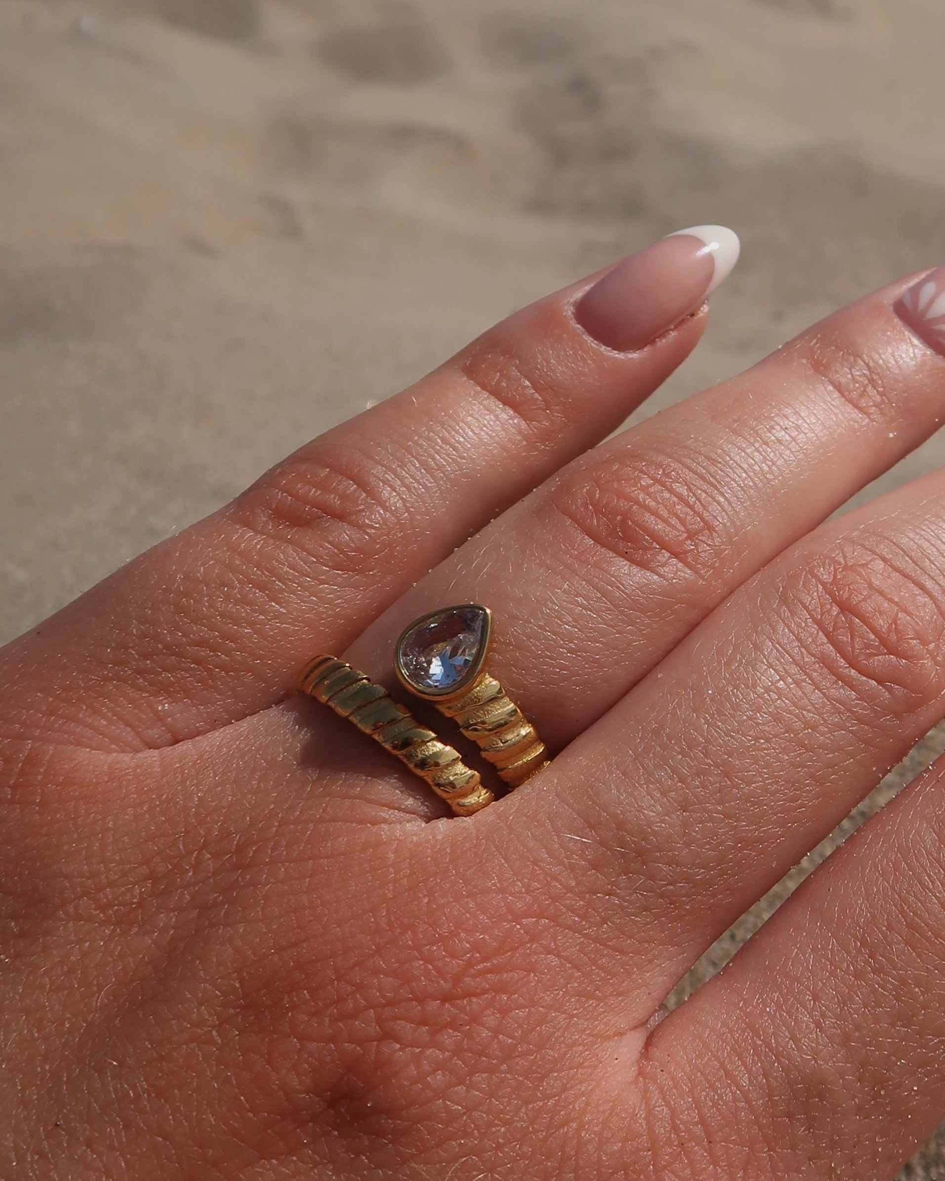 Gouden spiraalvormige ring met reliëf en zilverkleurige druppelvormige steen aan het uiteinde, gemaakt van stainless steel