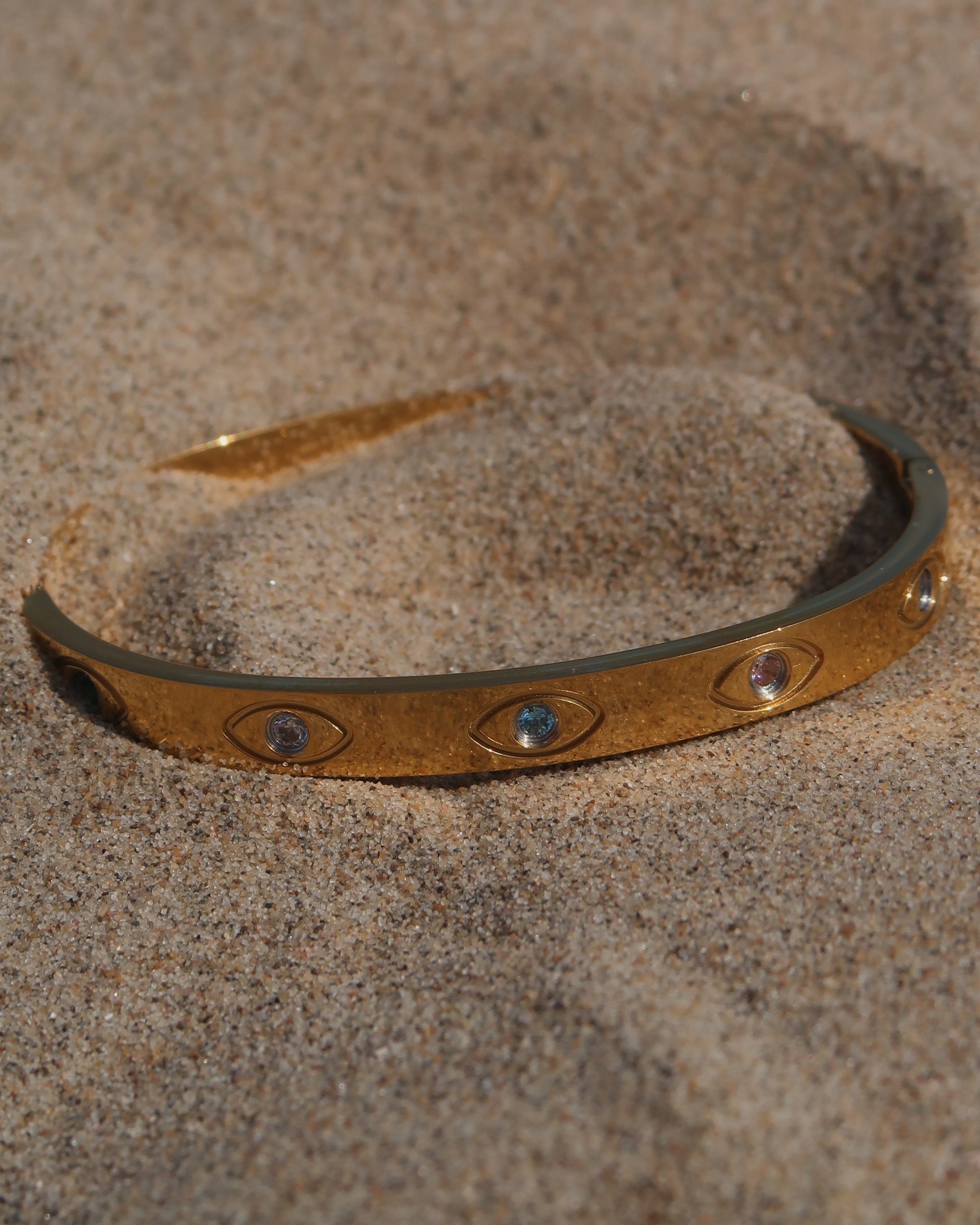 Gouden bangle met kleurrijke oogdetails en steentjes, gemaakt van stainless steel