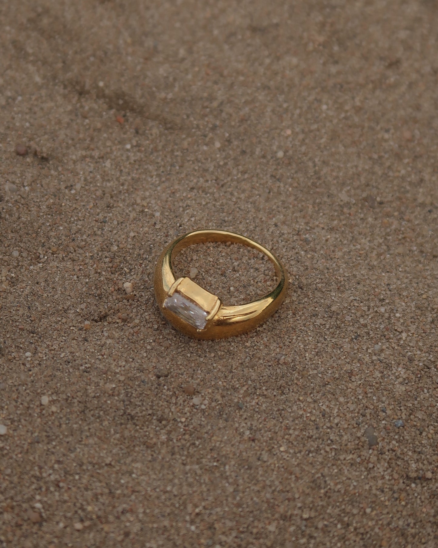 Gouden ring met glad design en een zilverkleurige steen aan de bovenzijde, gemaakt van waterproof stainless steel.