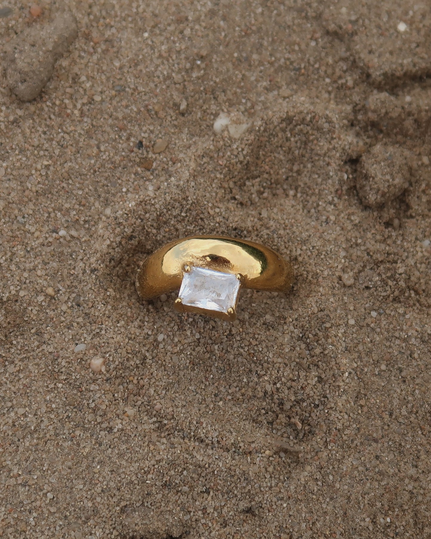 Gouden ring met glad design en een zilverkleurige steen aan de bovenzijde, gemaakt van waterproof stainless steel.