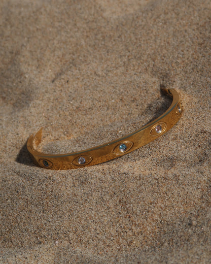 Gouden bangle met kleurrijke oogdetails en steentjes, gemaakt van stainless steel