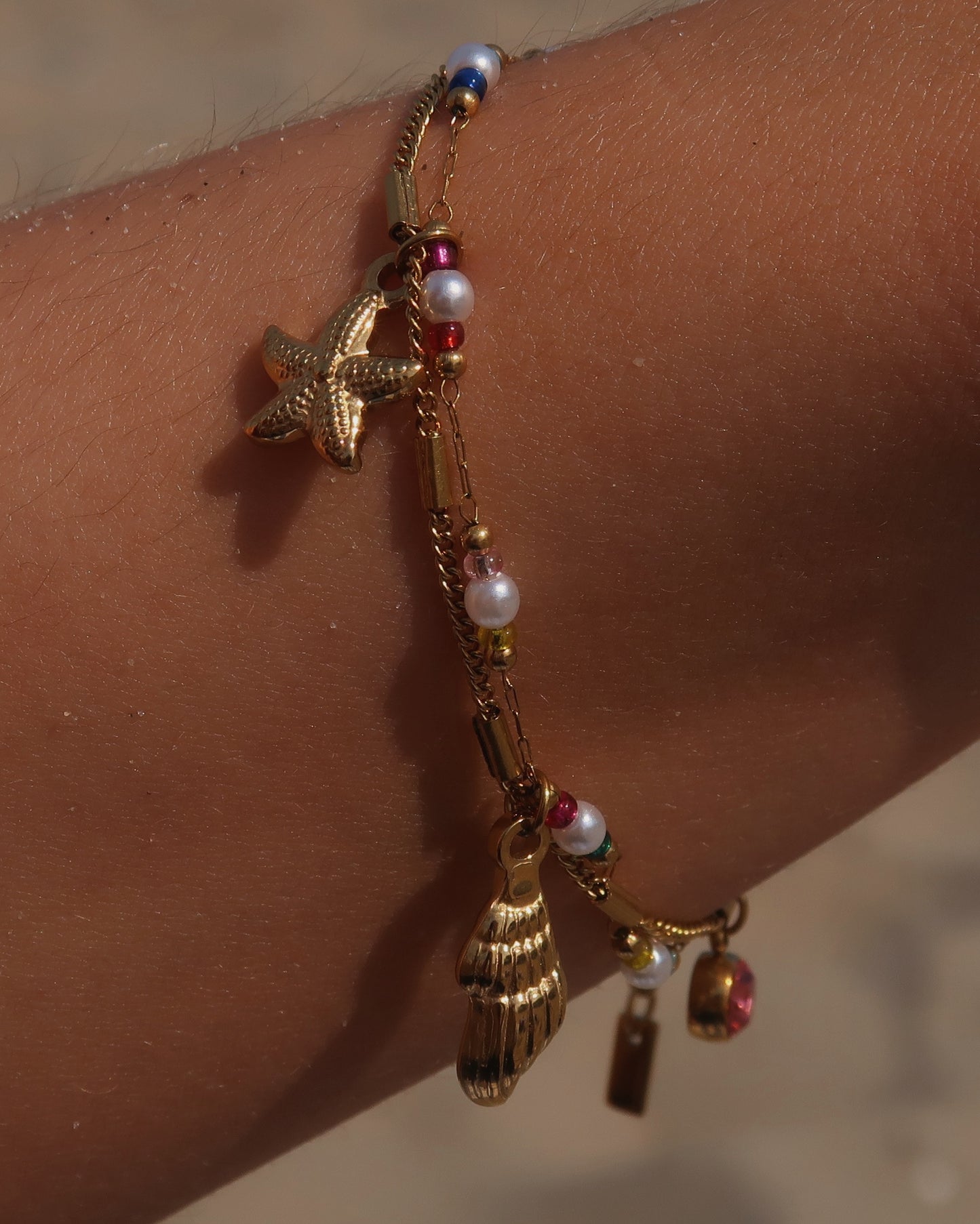 Gouden stainless steel armband met kleurrijke kraaltjes en bedels in de vorm van een schelp, zeester en roze steen – zomerse sieradenstijl.