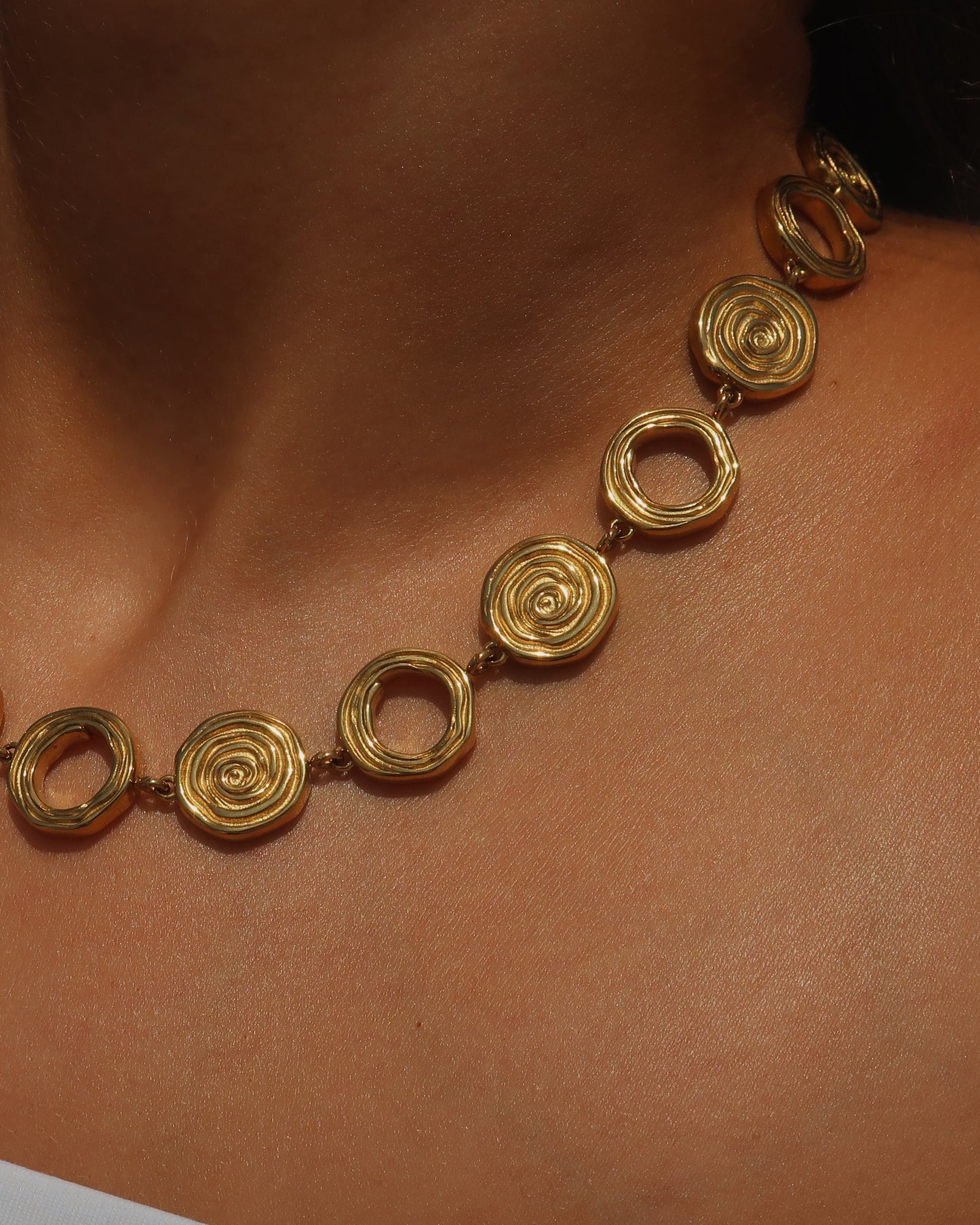 Gouden statementketting met aaneengeschakelde ronde schelpvormen in verschillende stijlen.

