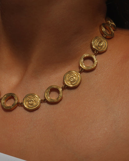 Gouden statementketting met aaneengeschakelde ronde schelpvormen in verschillende stijlen.

