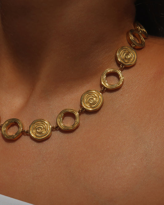 Gouden statementketting met aaneengeschakelde ronde schelpvormen in verschillende stijlen.

