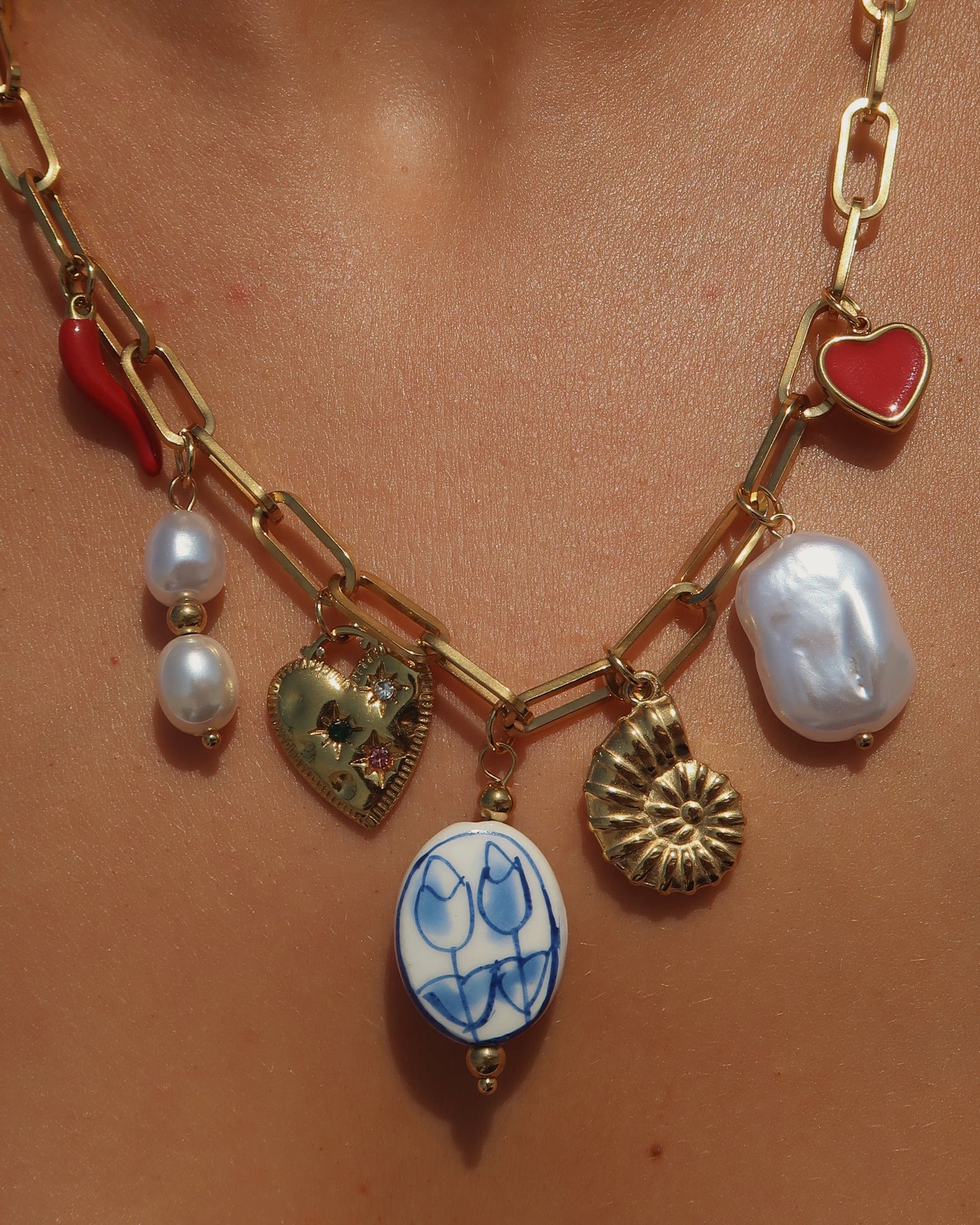 Gouden ketting met zeven bedels, waaronder een chilipeper, hartje en schelp – kleurrijk en speels ontwerp