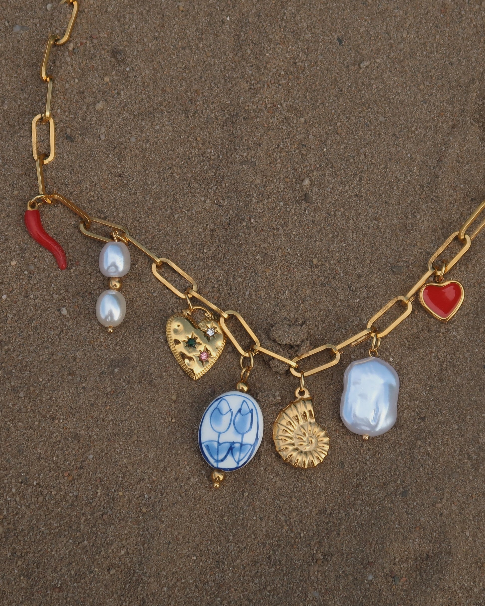 Gouden ketting met zeven bedels, waaronder een chilipeper, hartje en schelp – kleurrijk en speels ontwerp