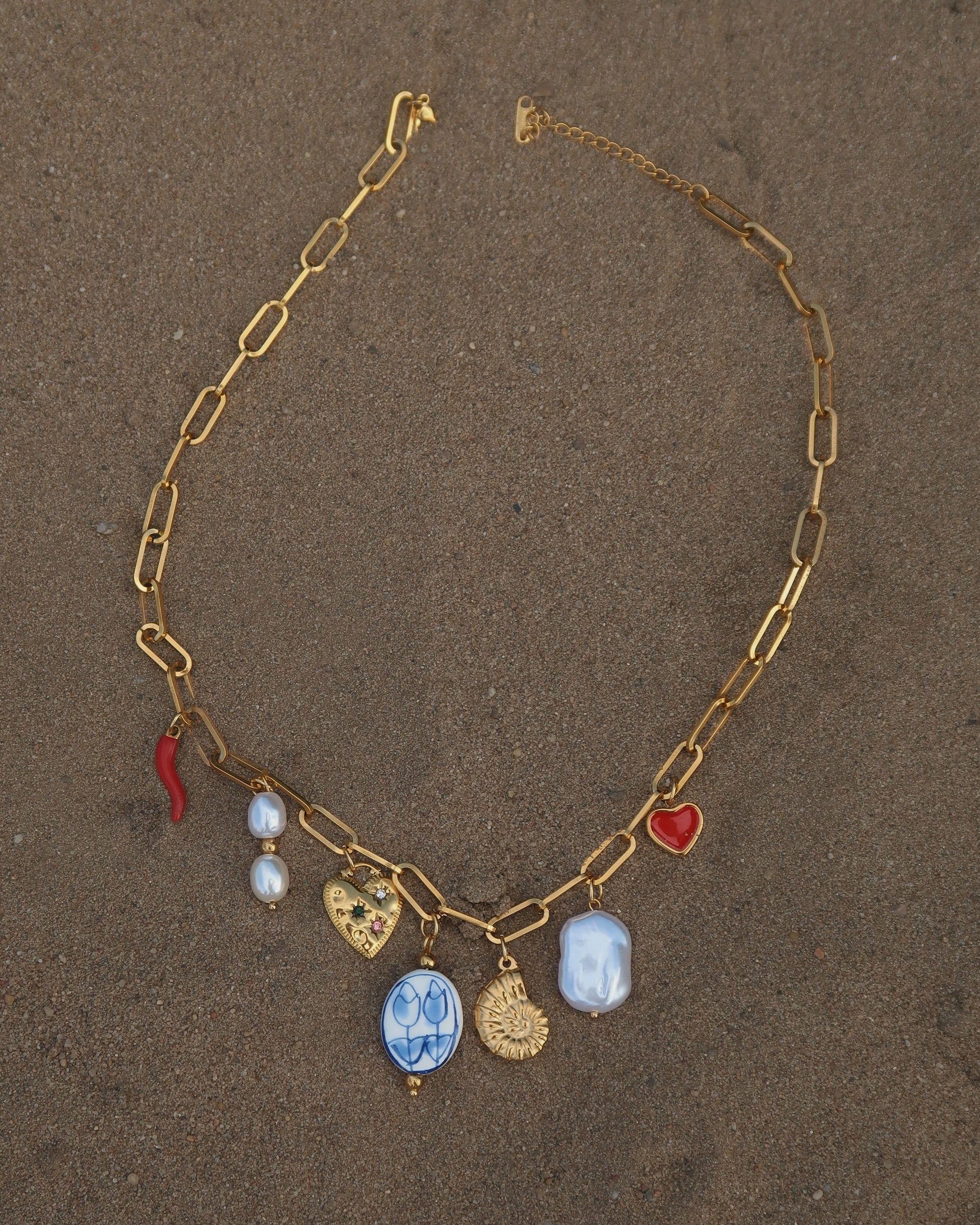Gouden ketting met zeven bedels, waaronder een chilipeper, hartje en schelp – kleurrijk en speels ontwerp