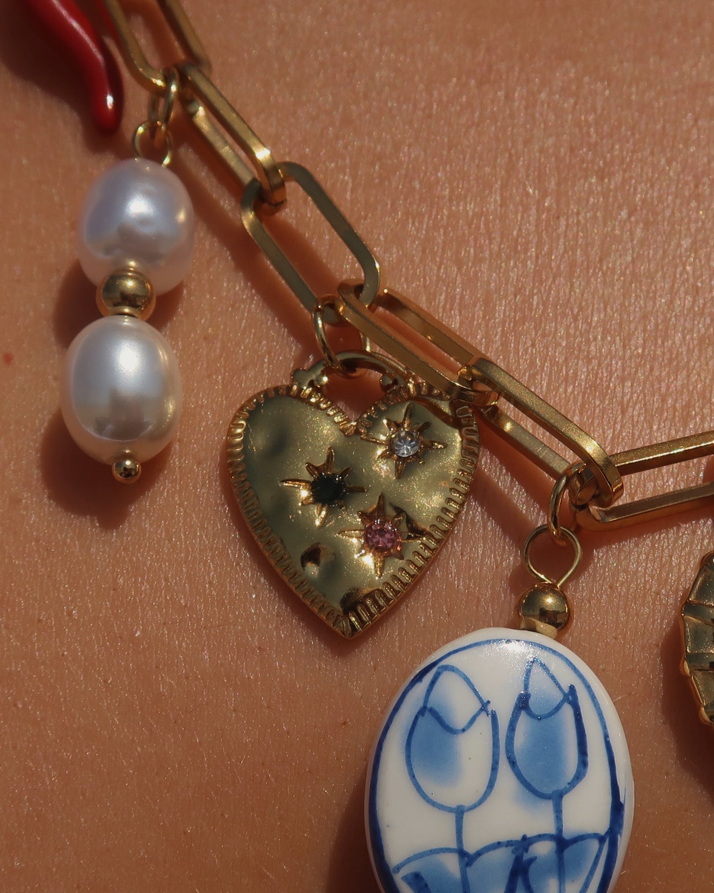 Gouden ketting met zeven bedels, waaronder een chilipeper, hartje en schelp – kleurrijk en speels ontwerp