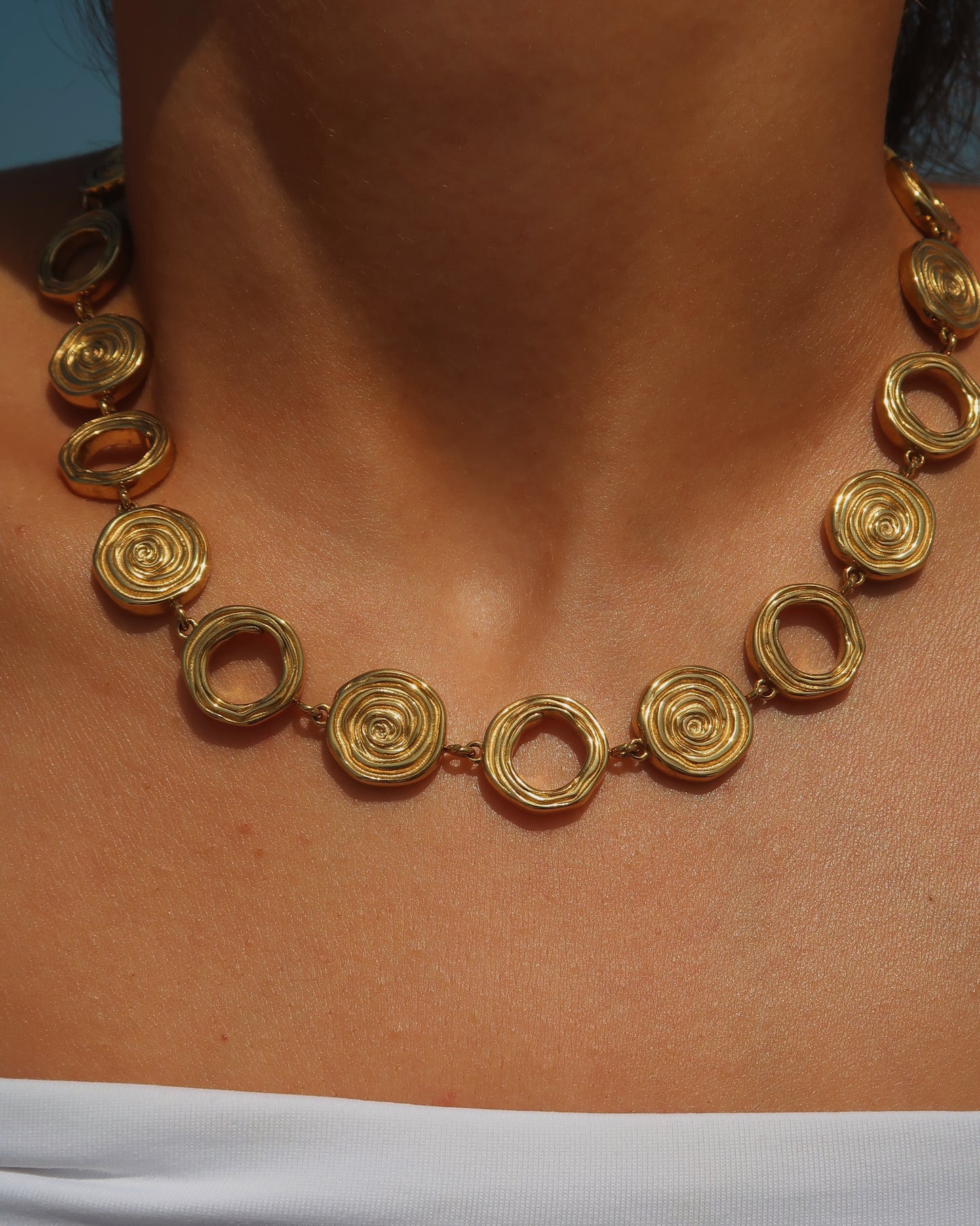 Gouden statementketting met aaneengeschakelde ronde schelpvormen in verschillende stijlen.