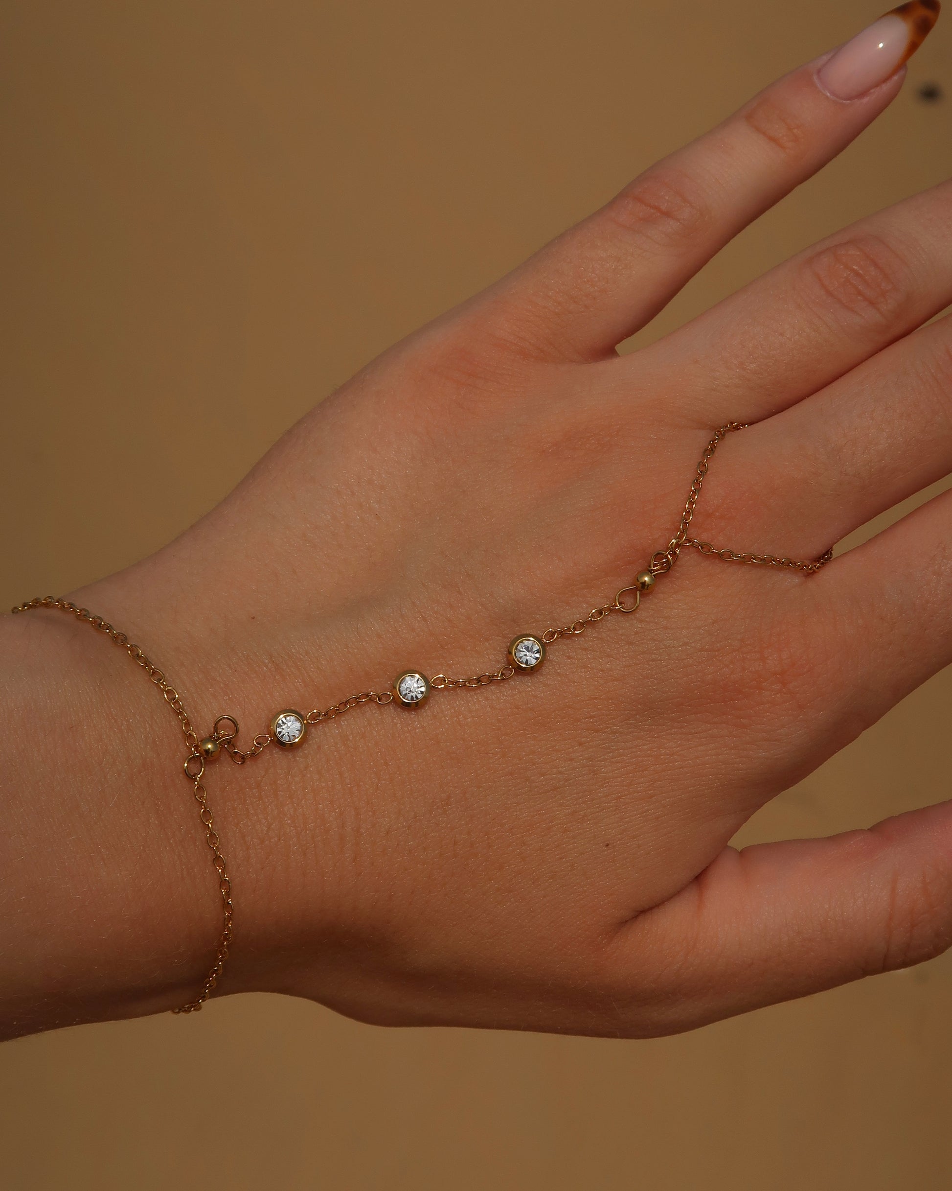 Lume Hand Chain armband voor hand en pols, verkrijgbaar in goud en zilver, stainless steel, waterproof, met drie subtiele steentjes, verstelbaar en ook verkrijgbaar als sieradenset met bijpassende ketting.

