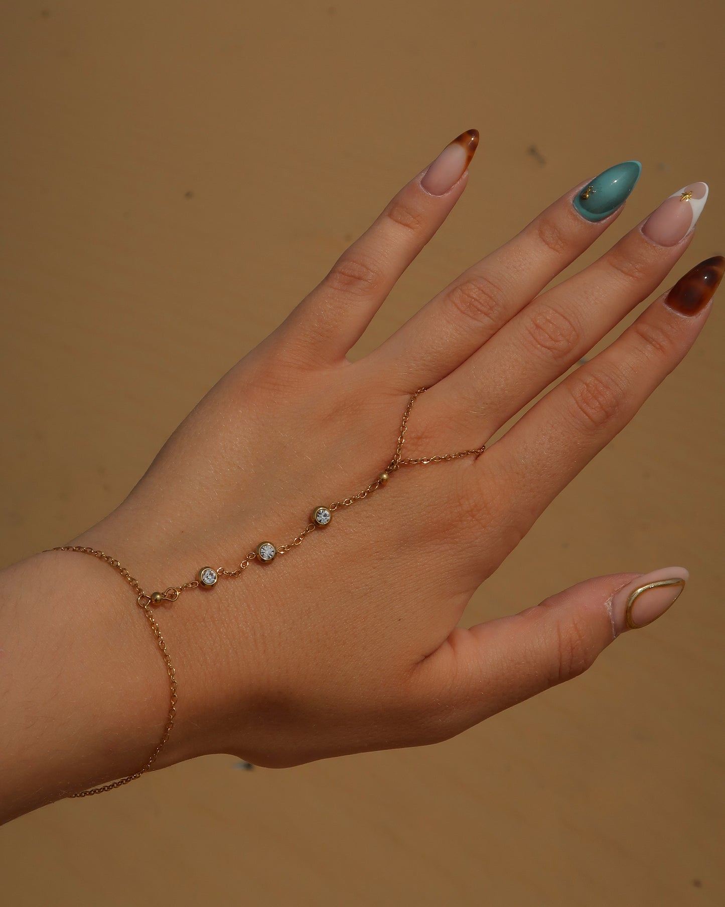 Lume Hand Chain armband voor hand en pols, verkrijgbaar in goud en zilver, stainless steel, waterproof, met drie subtiele steentjes, verstelbaar en ook verkrijgbaar als sieradenset met bijpassende ketting.