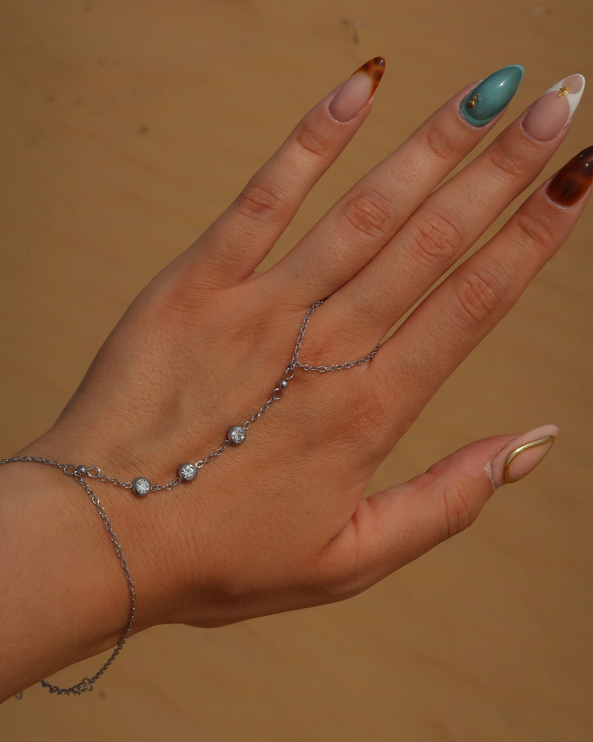 Lume Hand Chain armband voor hand en pols, verkrijgbaar in goud en zilver, stainless steel, waterproof, met drie subtiele steentjes, verstelbaar en ook verkrijgbaar als sieradenset met bijpassende ketting.