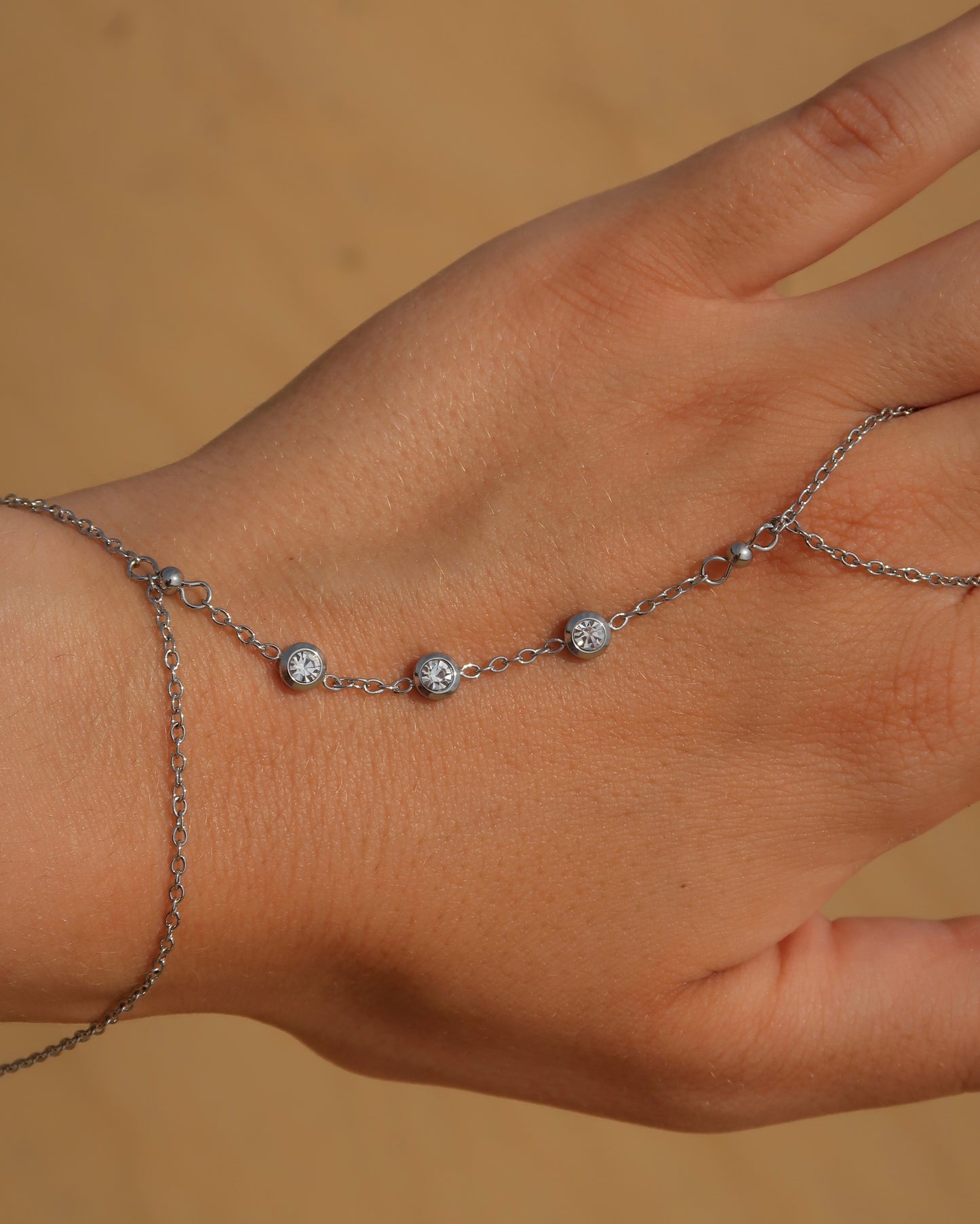 Lume Hand Chain armband voor hand en pols, verkrijgbaar in goud en zilver, stainless steel, waterproof, met drie subtiele steentjes, verstelbaar en ook verkrijgbaar als sieradenset met bijpassende ketting.